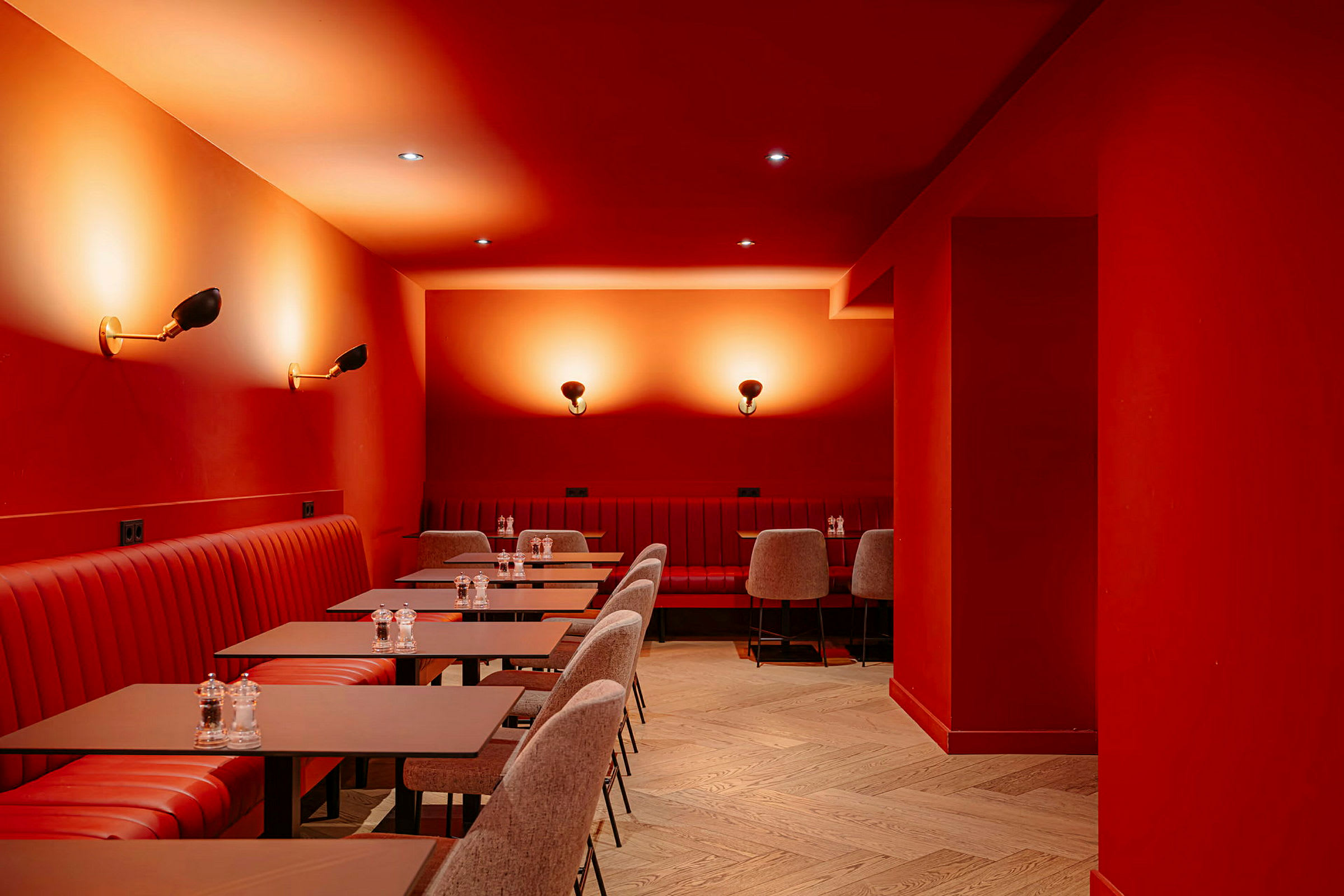 Bilde av interiøret i en restaurant eller kafé med røde vegger og tak. Rød polstring på sitteplassene og matchende bord. Belysning med vegglamper skaper en varm atmosfære. (AI-generert tekst)