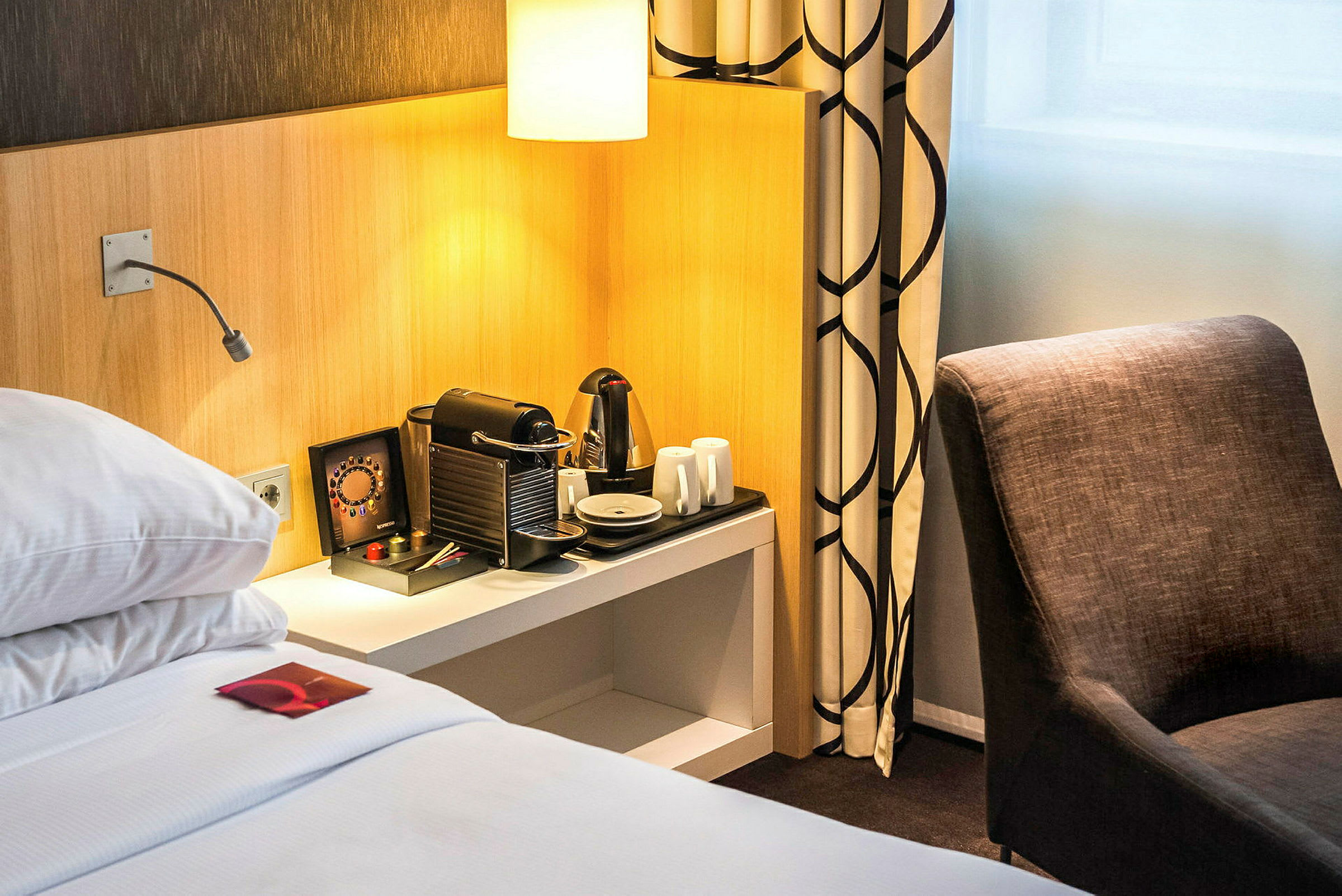 Hotellrom med seng, kaffemaskin og stol. (AI-generert tekst)