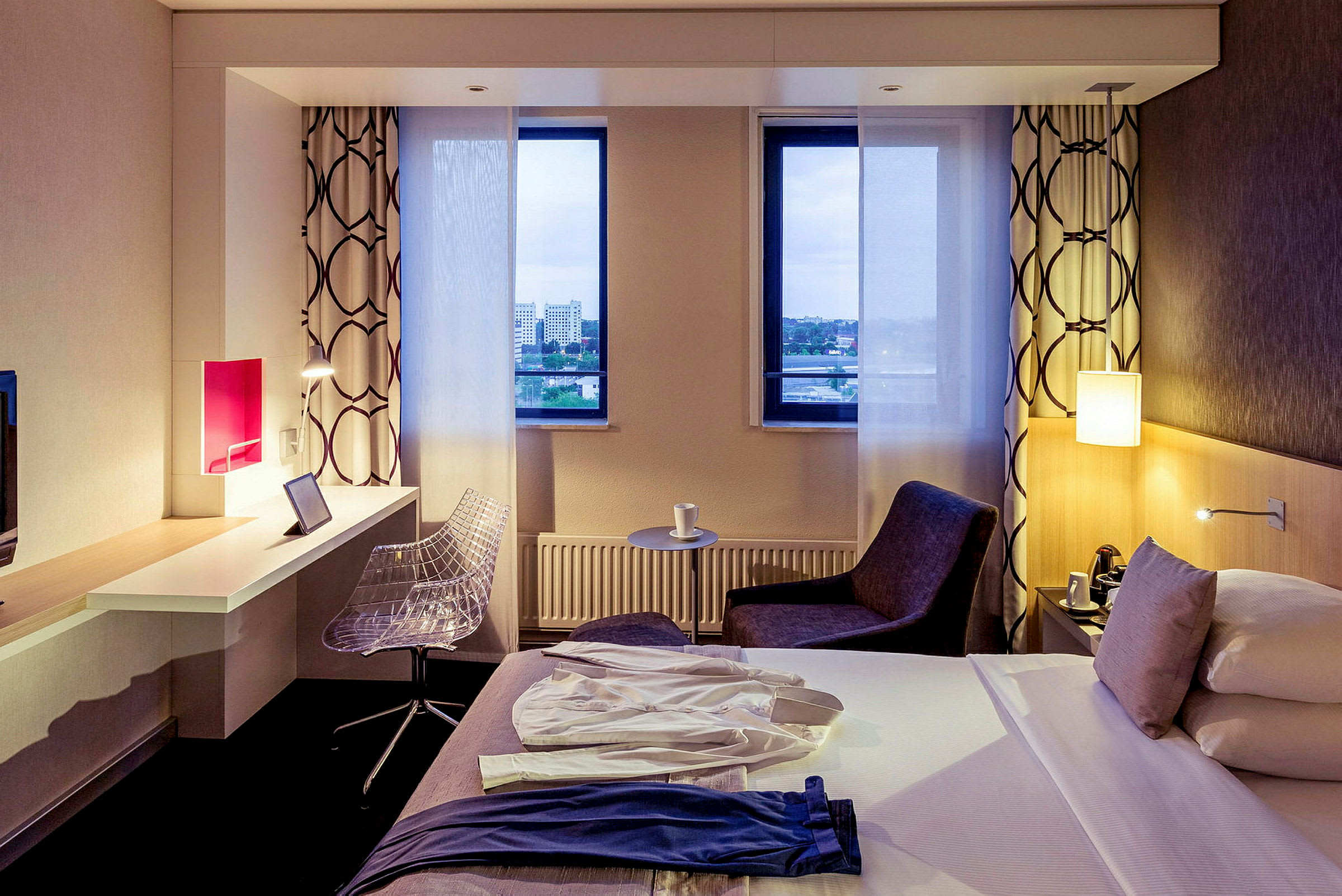 Et hotellrom med en seng, skrivebord og stol samt to vinduer med utsikt. (AI-generert tekst)