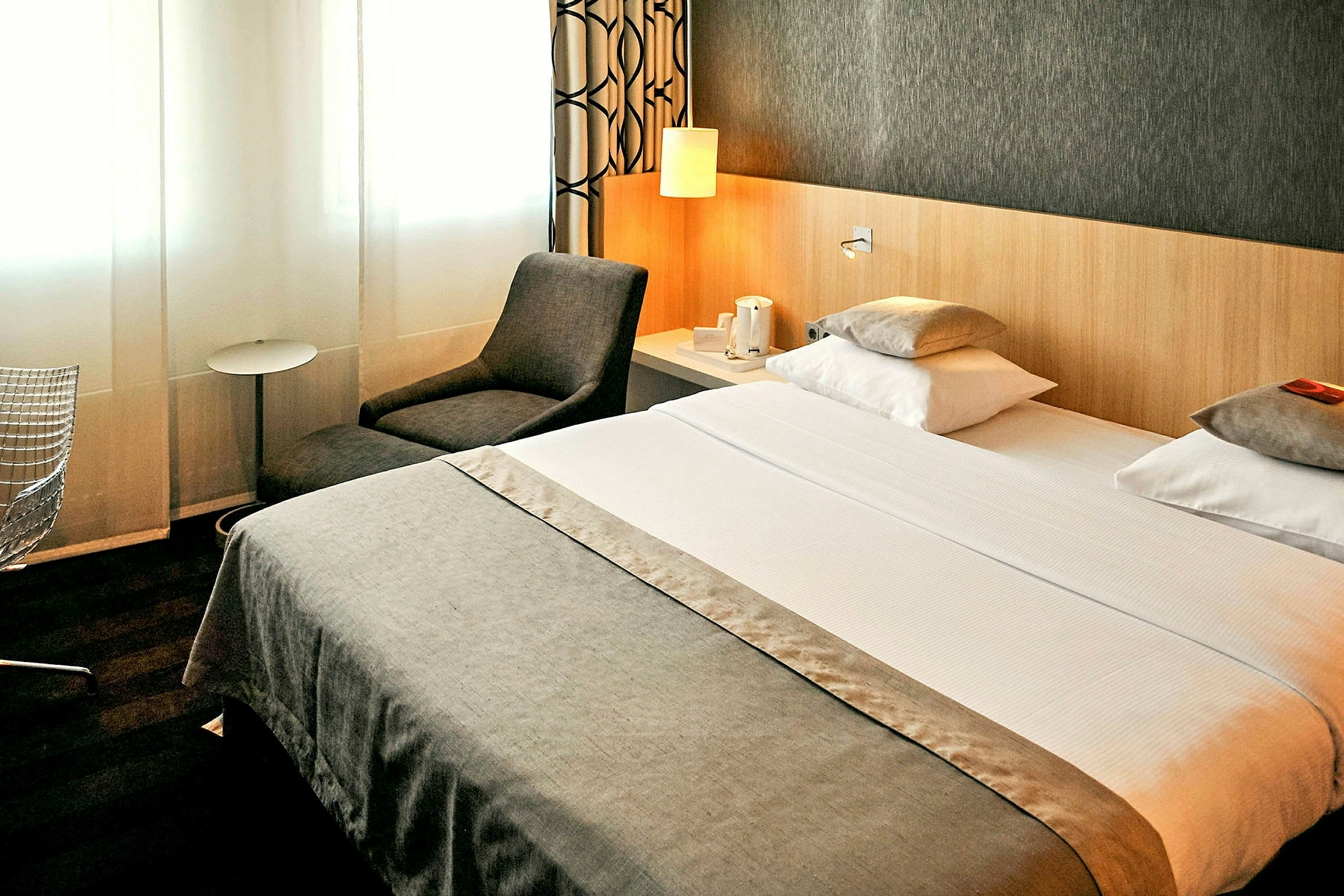 Hotellrom med dobbeltseng, lenestol og sidebord. (AI-generert tekst)