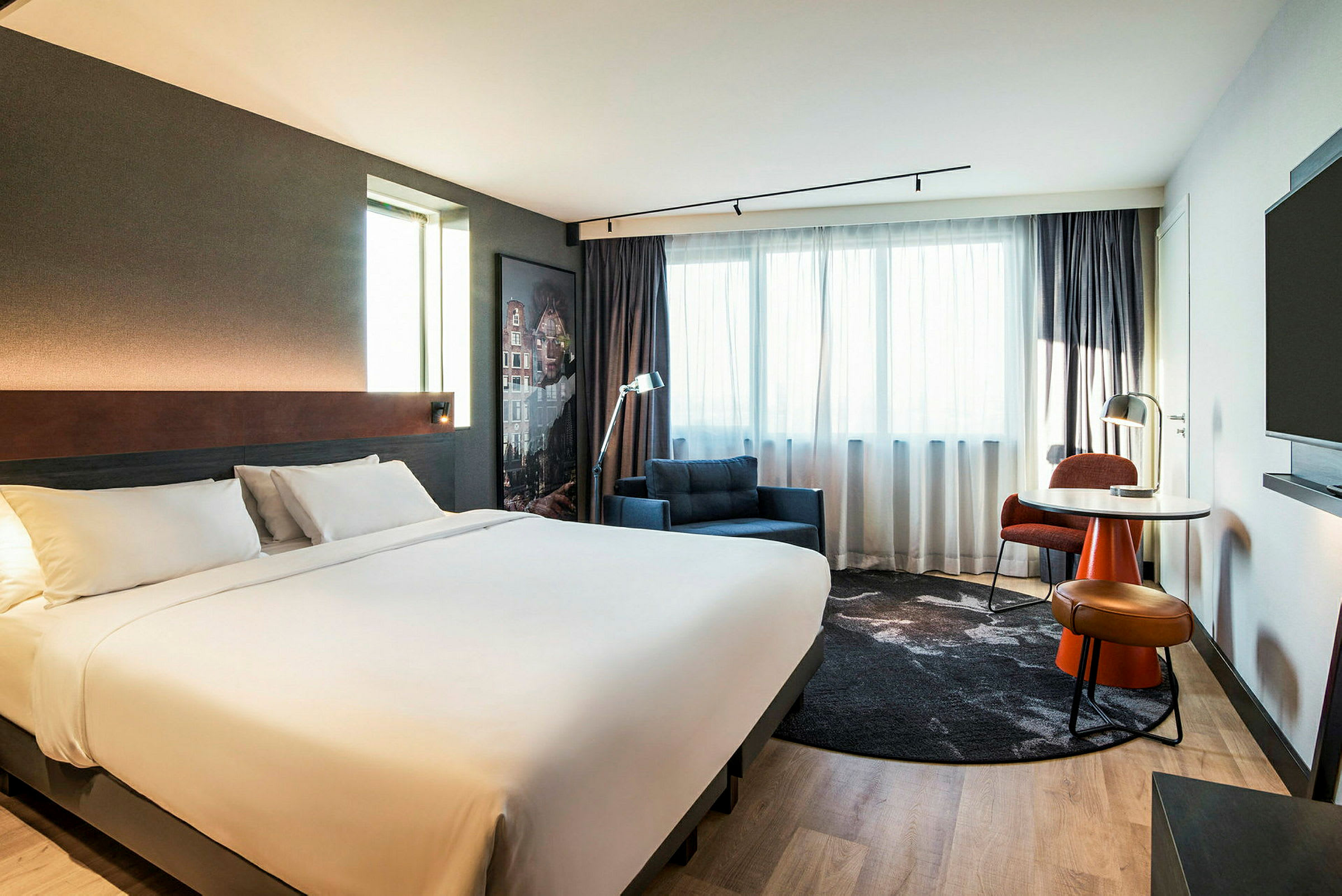 Et moderne hotellrom med en stor dobbeltseng, lenestol og et skrivebord ved vinduet. (AI-generert tekst)