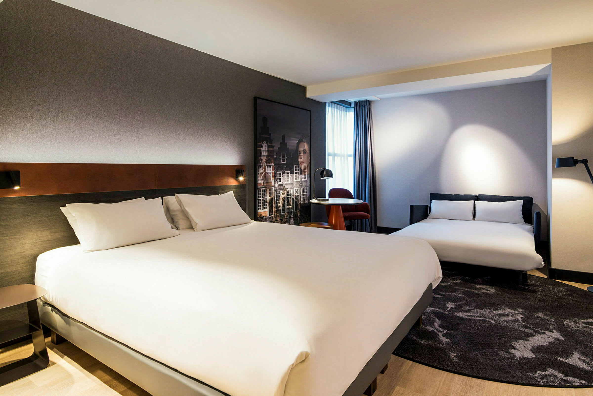 Hotellrom med to senger og et lite bord med en stol ved et vindu. (AI-generert tekst)