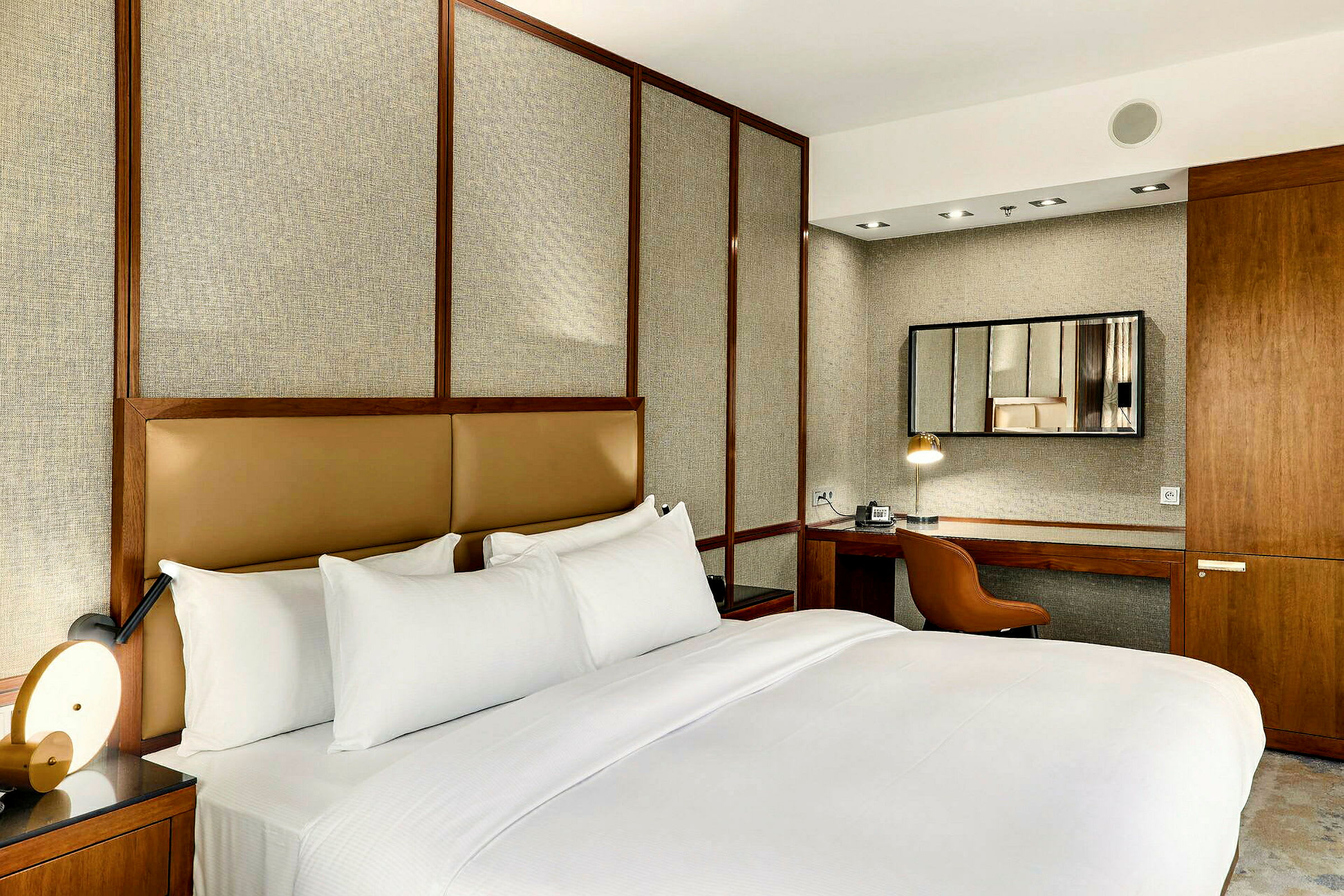 Et elegant og stilrent hotellrom med en stor dobbeltseng, minimalistisk innredning og et skrivebord med speil. (AI-generert tekst)