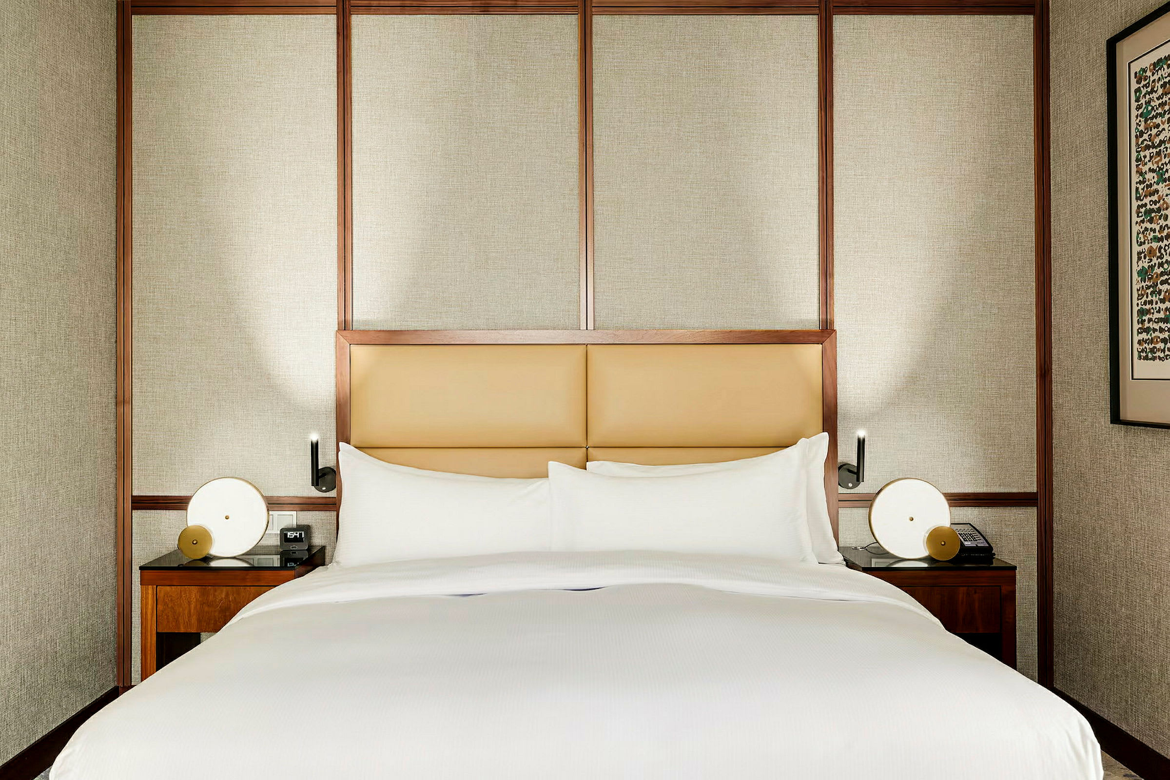 En seng med hvitt sengetøy og en stoppet hodegavl, omgitt av elegante trepaneler. To nattbord med lamper og et bilde på veggen. (AI-generert tekst)