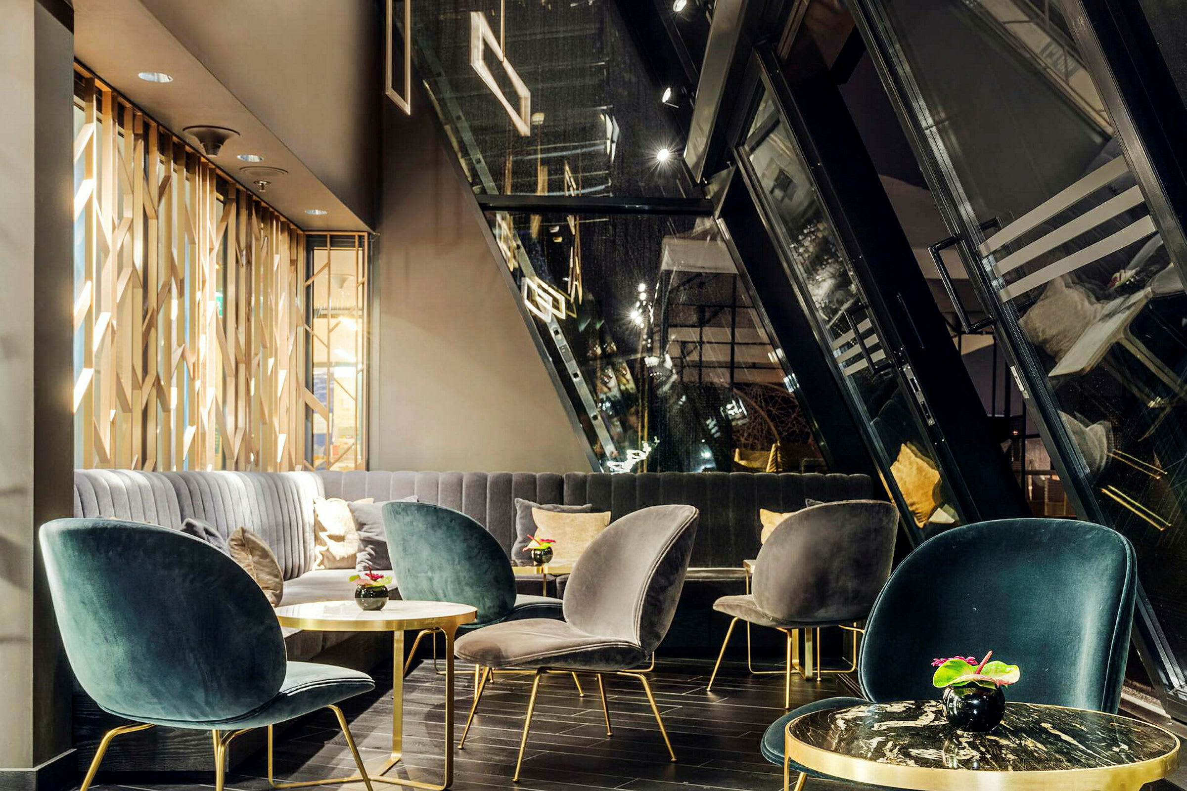Et moderne stue eller loungeområde med elegante sete i fløyel, små bord med metallrammer og dekorative planter, samt store vinduer som heller innover. (AI-generert tekst)