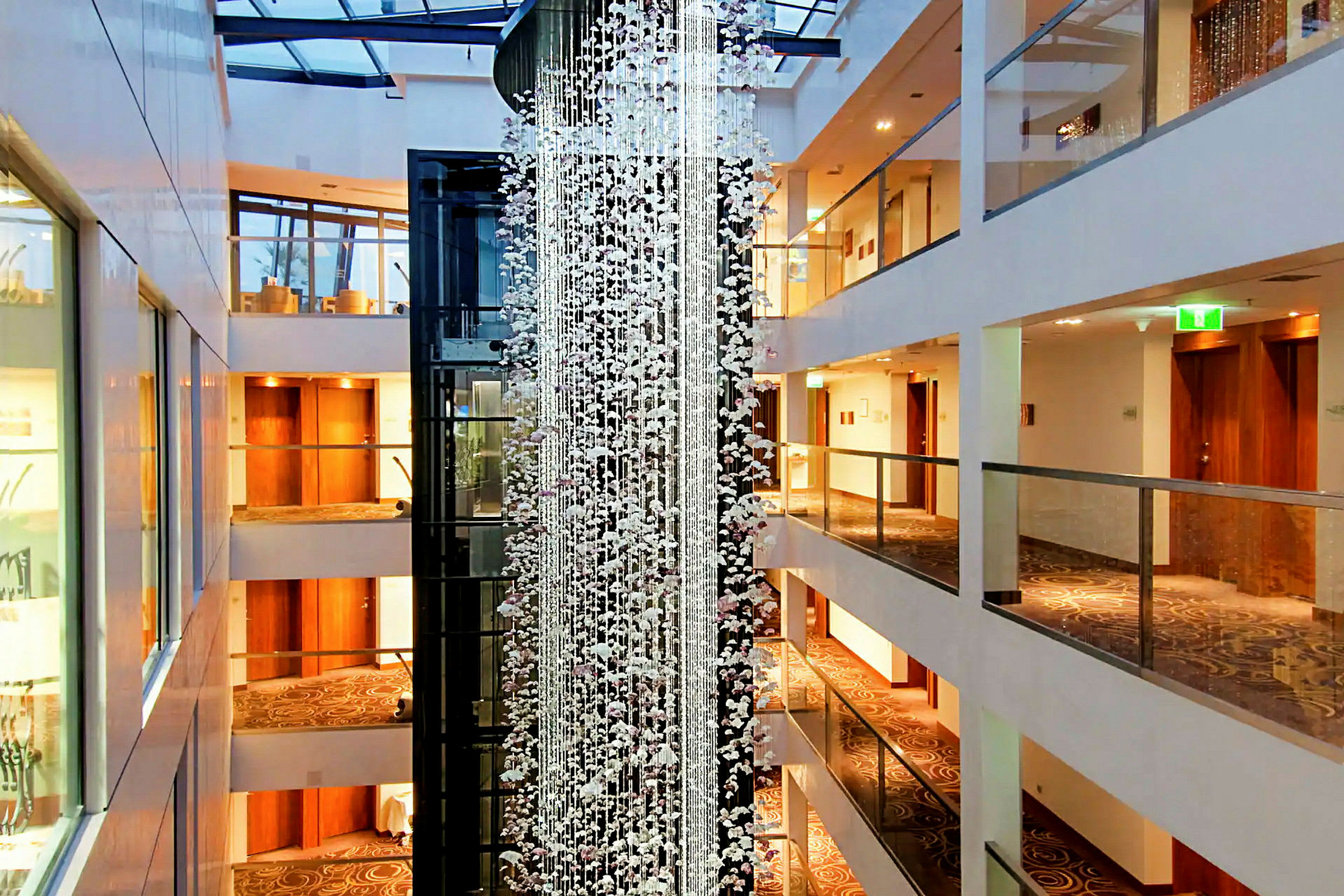 Et hotellfoajé med flere etasjer, dekorert med en glasthengende installasjon og varme lyse farger. (AI-generert tekst)