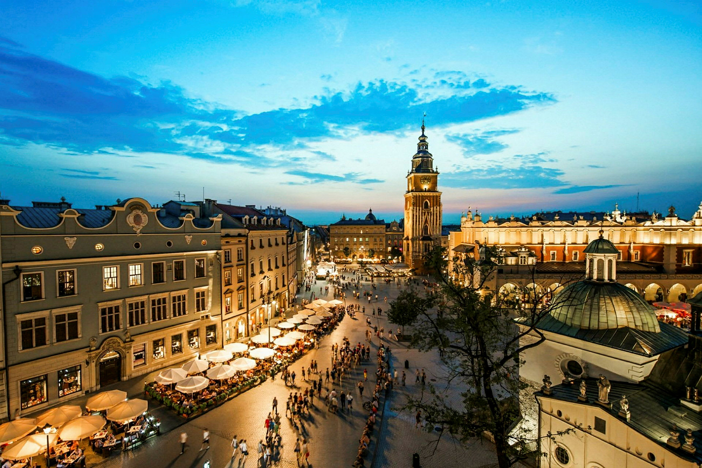Et stort torg med historiske bygninger og et kirketårn i skumringslys. (AI-generert tekst)