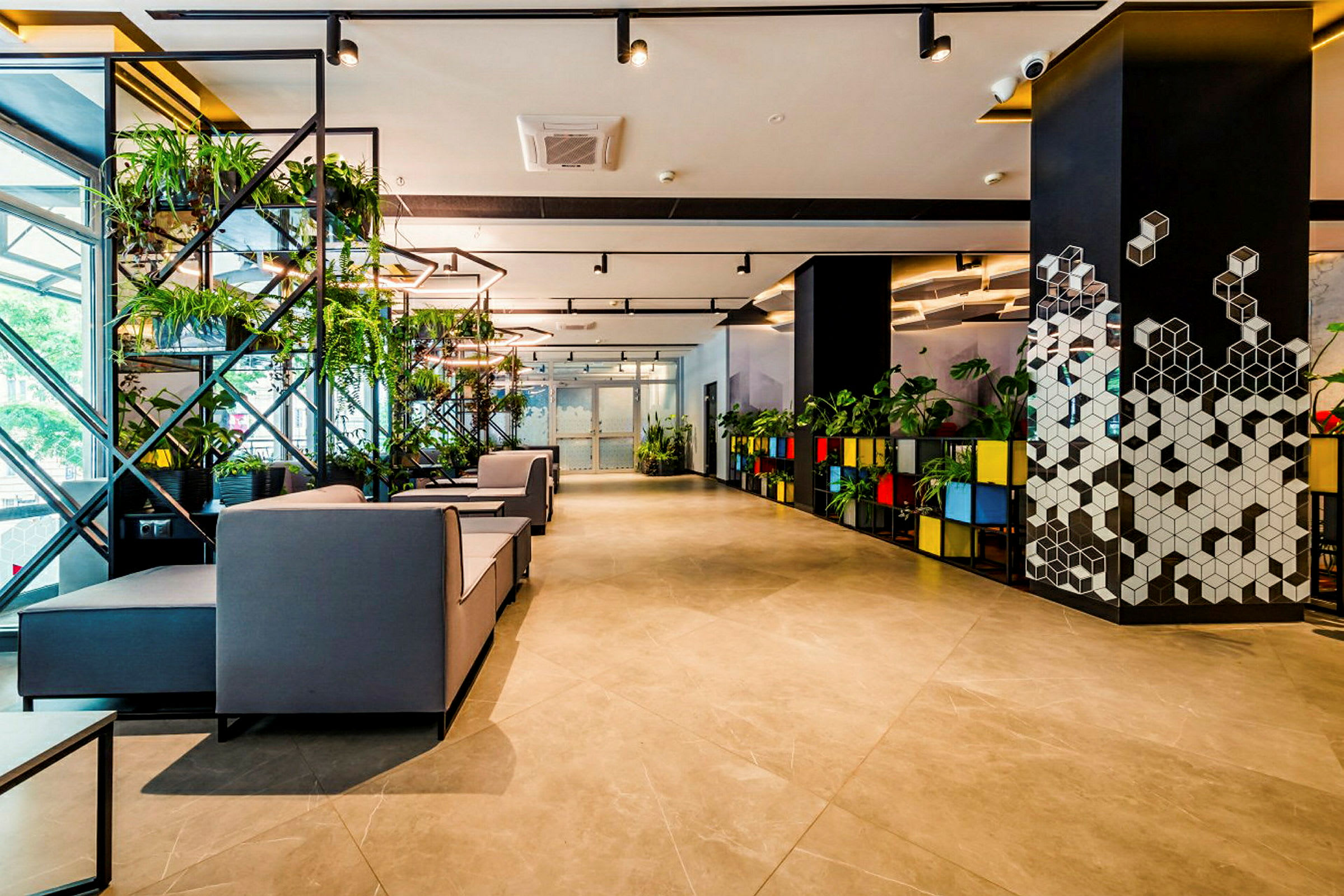 Et moderne rom med stilrent interiør, grå sofaer og planter på hyller. Gulvet er belagt med store fliser, og veggene har geometriske mønstre. (AI-generert tekst)