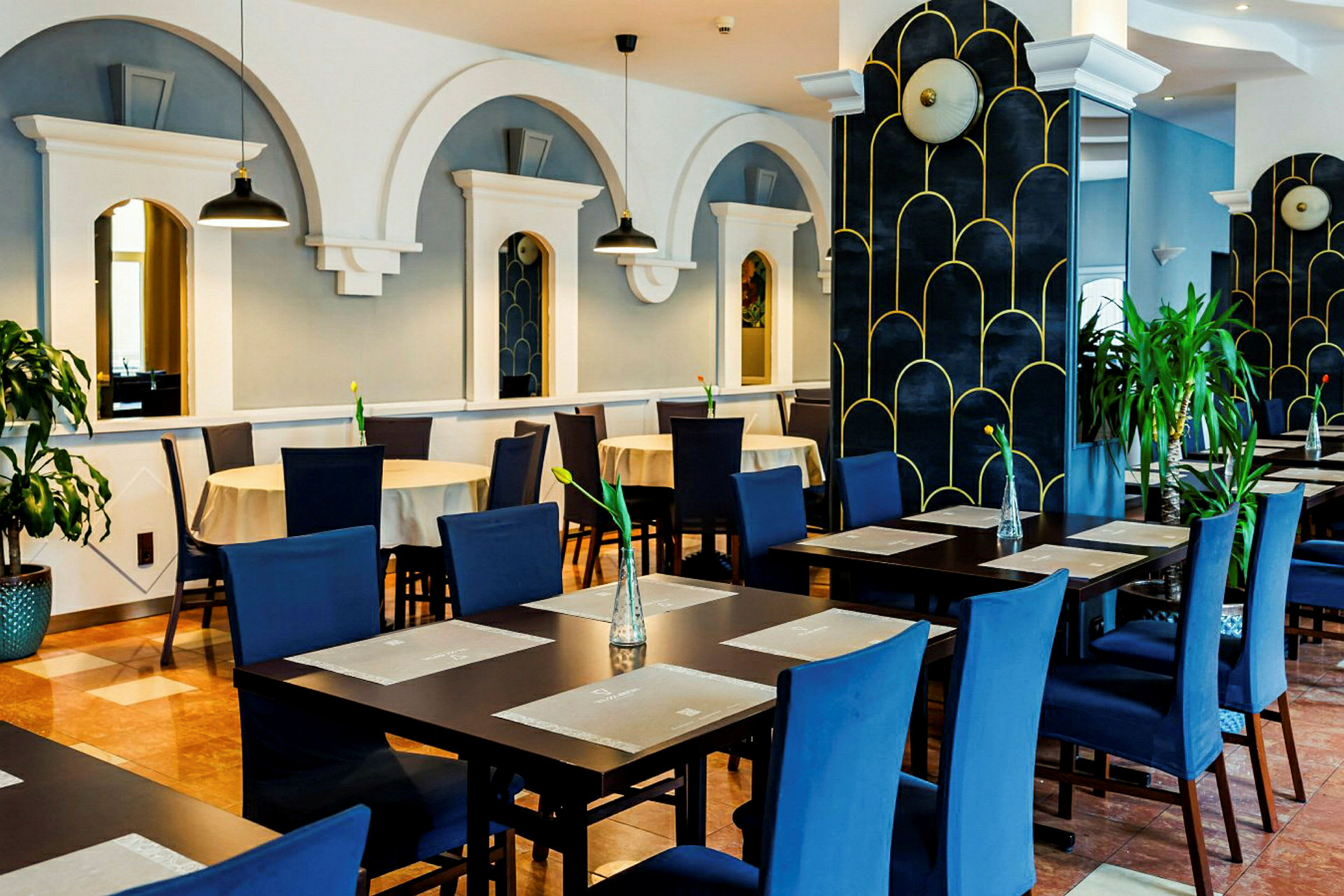 Restaurant med blå stoler, dekkede bord og dekorative buer på veggene. (AI-generert tekst)