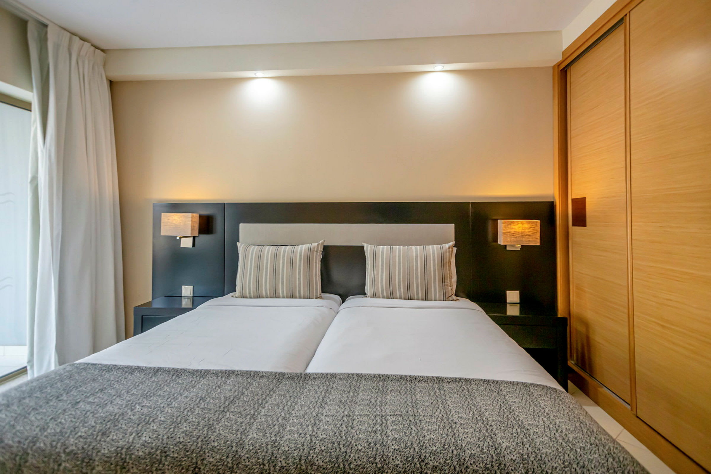 Bilde av et moderne hotellrom med en dobbeltseng, stripete puter og stilren innredning. (AI-generert tekst)