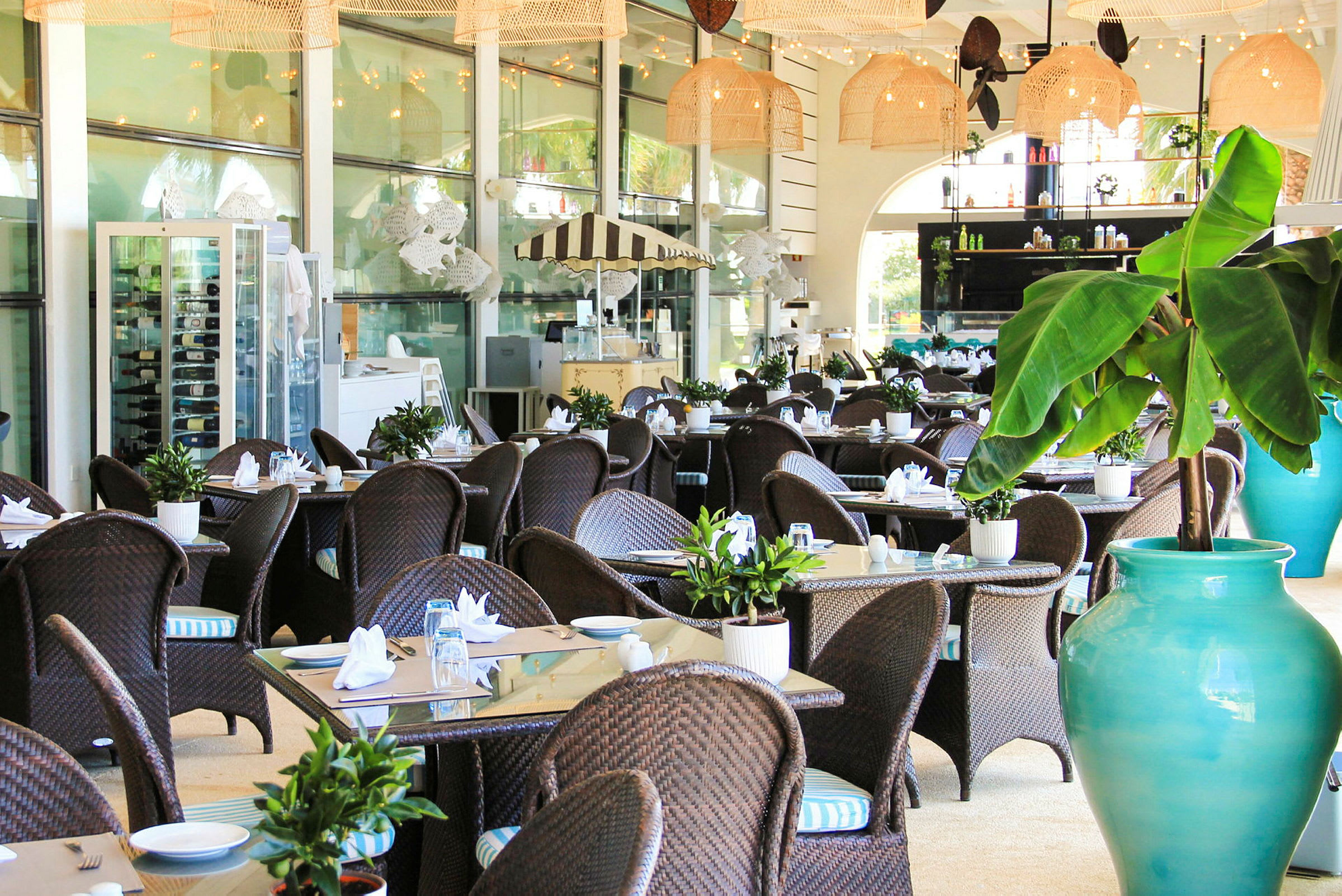 Bilde av en elegant restaurant med rottingmøbler og dekorerte bord, omgitt av planter og lys innredning. (AI-generert tekst)