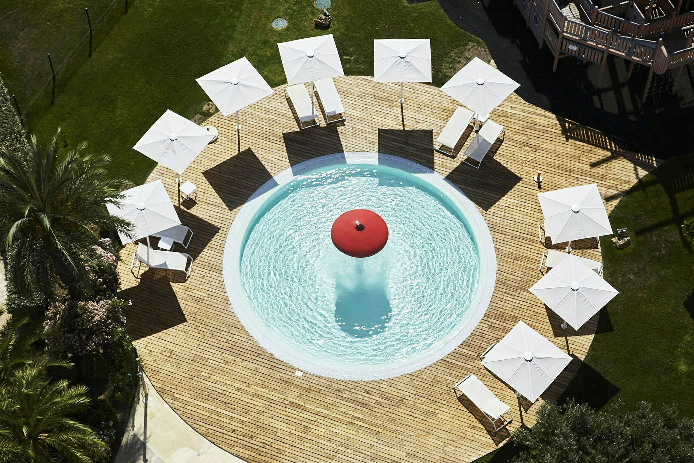 Et sirkulært basseng omgitt av treterrasse med solsenger og parasoller. (AI-generert tekst)