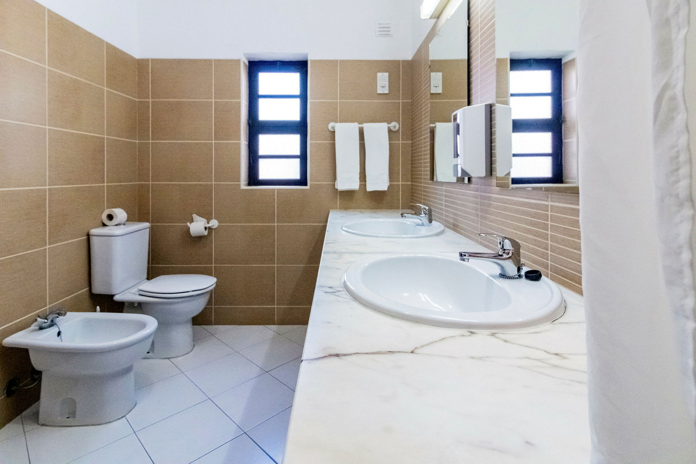 Bad med to vasker, toalett, bidet og vindu. (AI-generert tekst)
