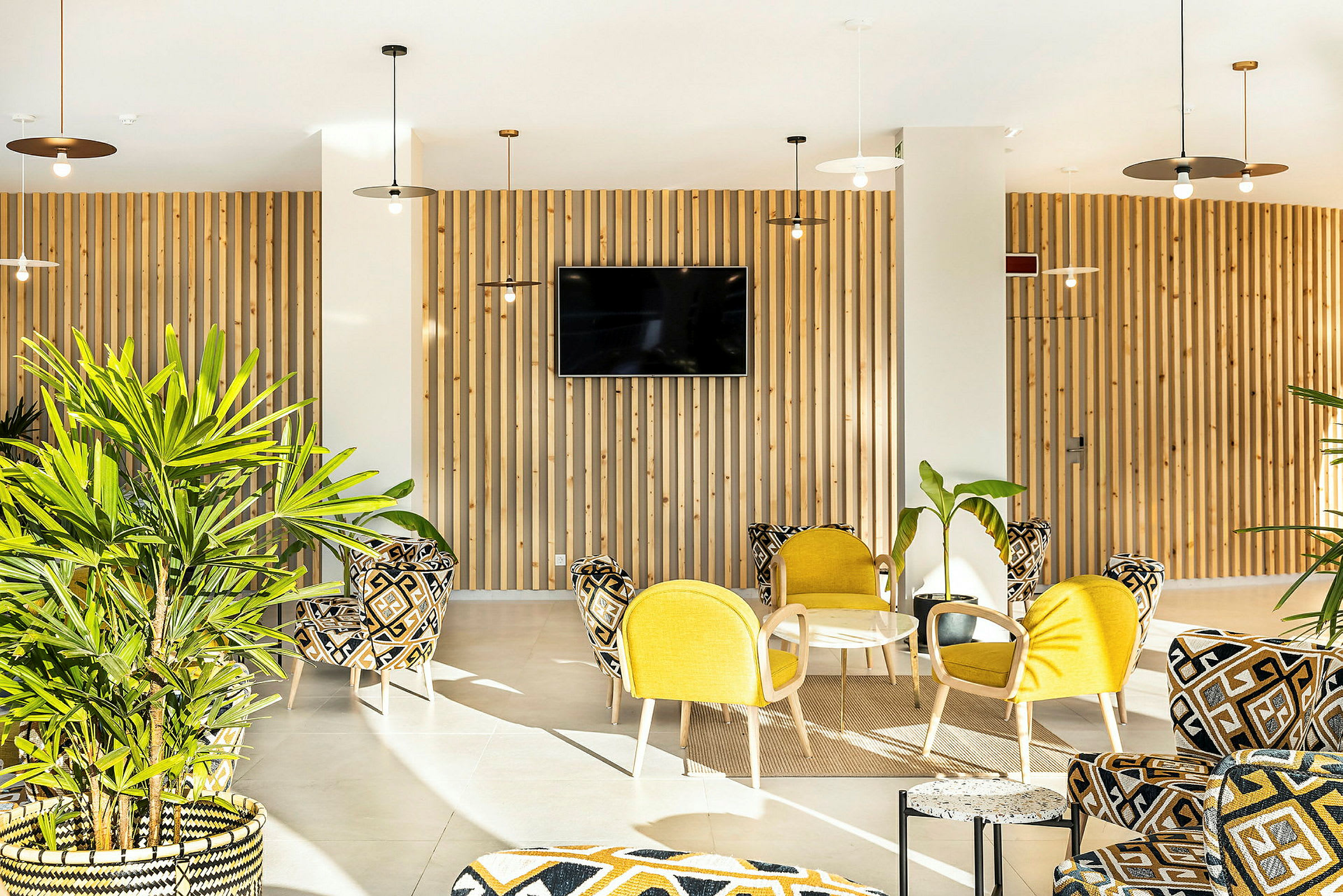 En lys og moderne lounge med gul og mønstret møblering og grønne planter. (AI-generert tekst)