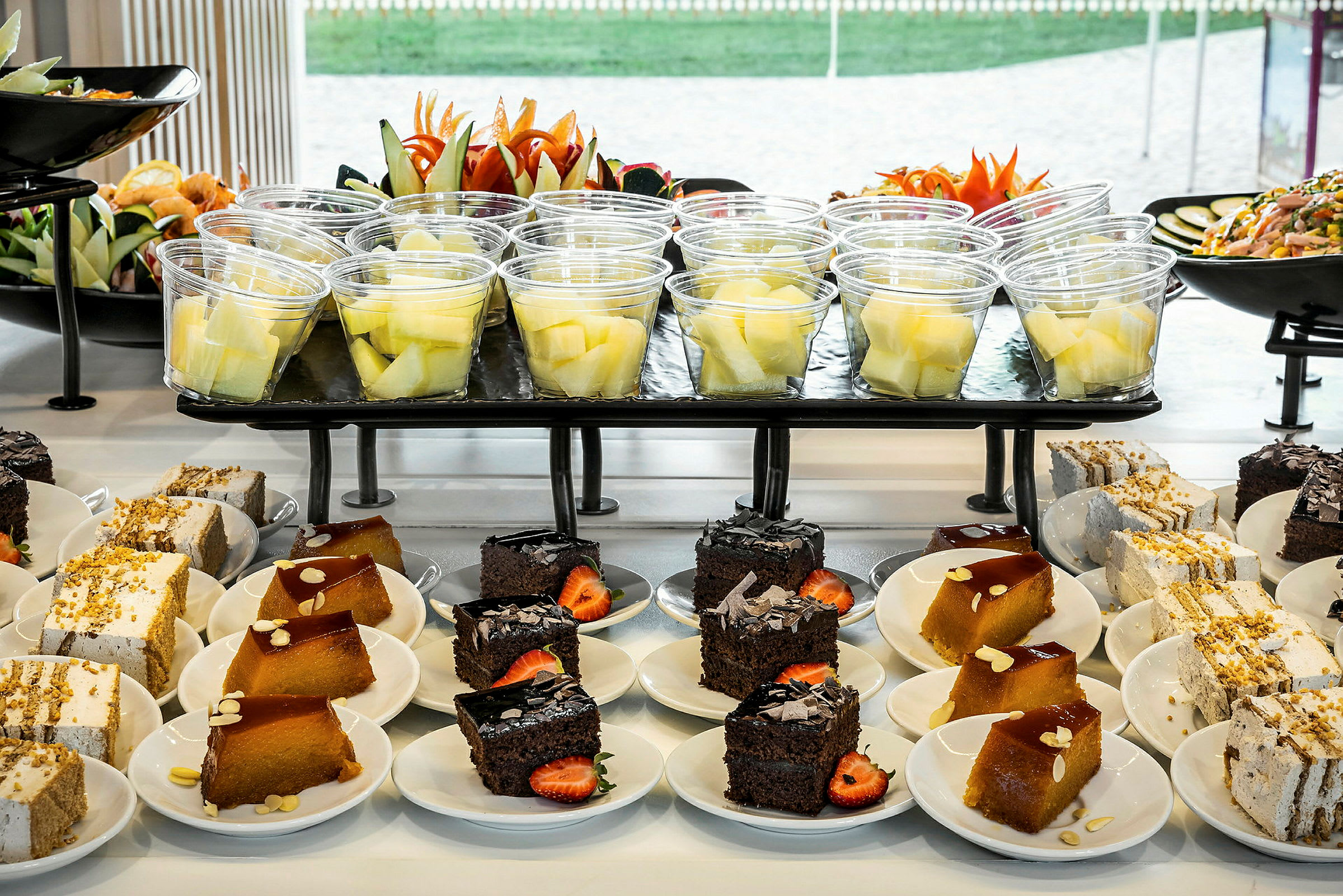 Buffet med desserter og fruktsalat arrangert på tallerkener og i plastglass. (AI-generert tekst)