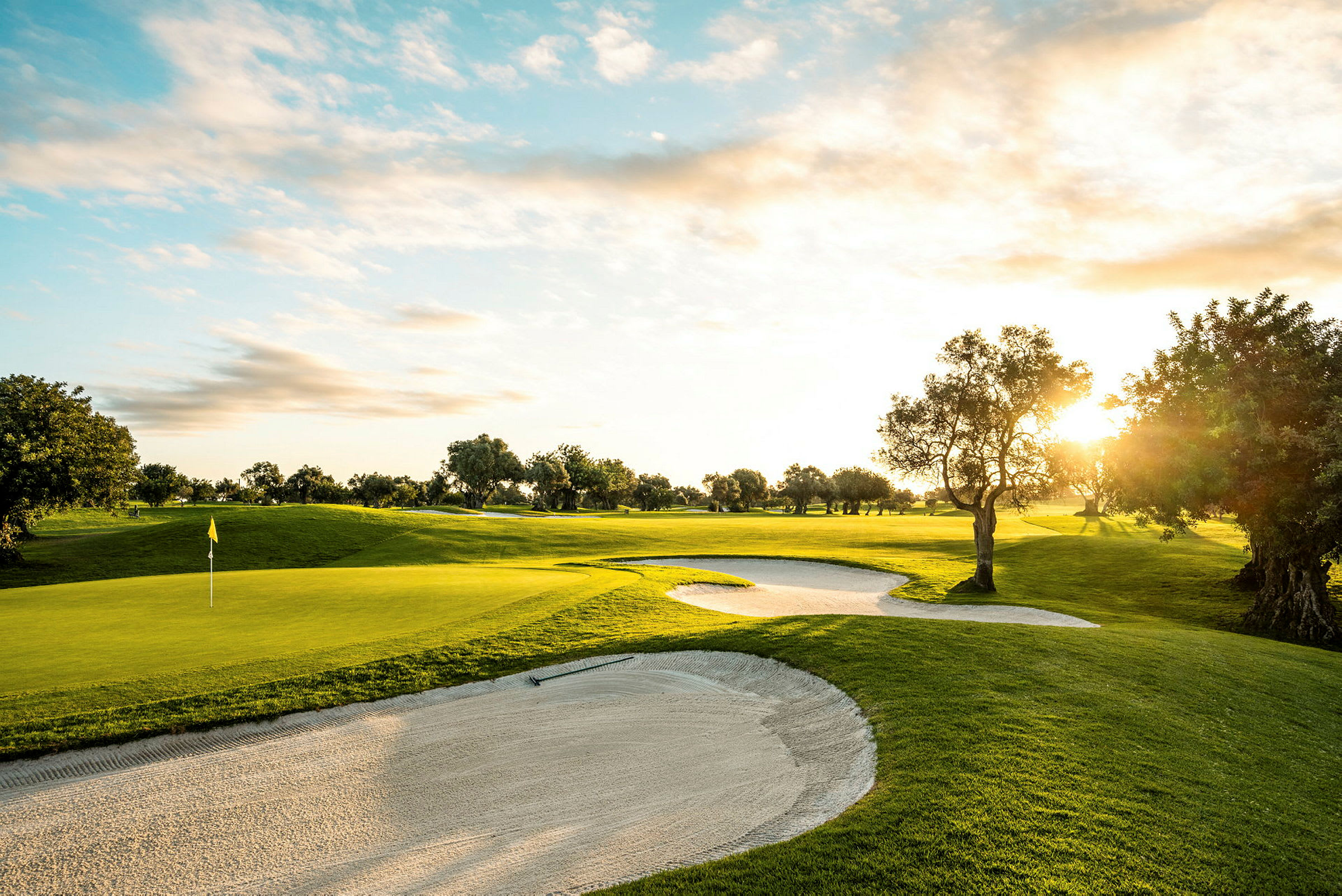En golfbane med sandbunkere, solnedgang og trær. (AI-generert tekst)