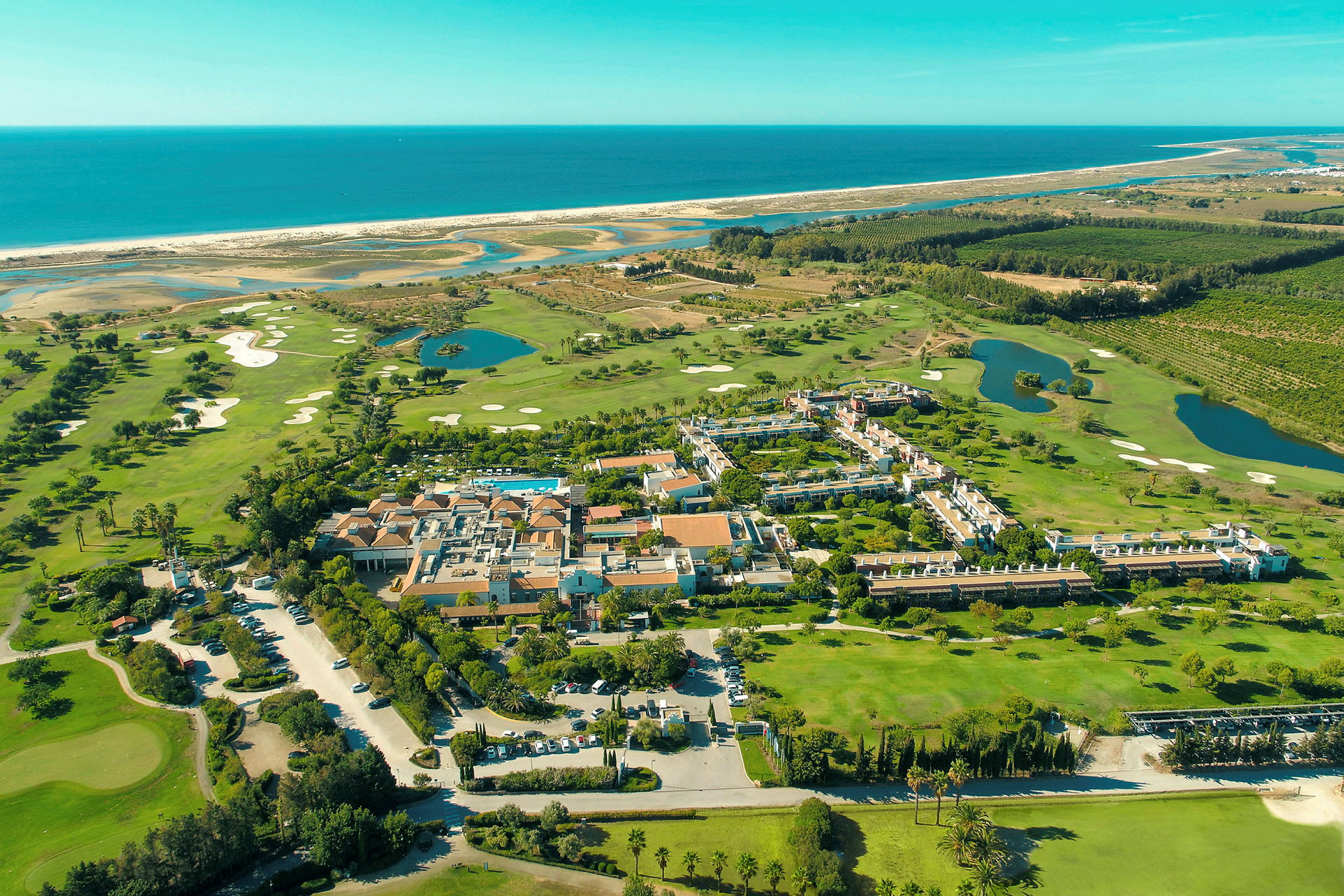 Flyfoto av en ferieanlegg omgitt av grøntområder, golfbaner og nærhet til havet. (AI-generert tekst)