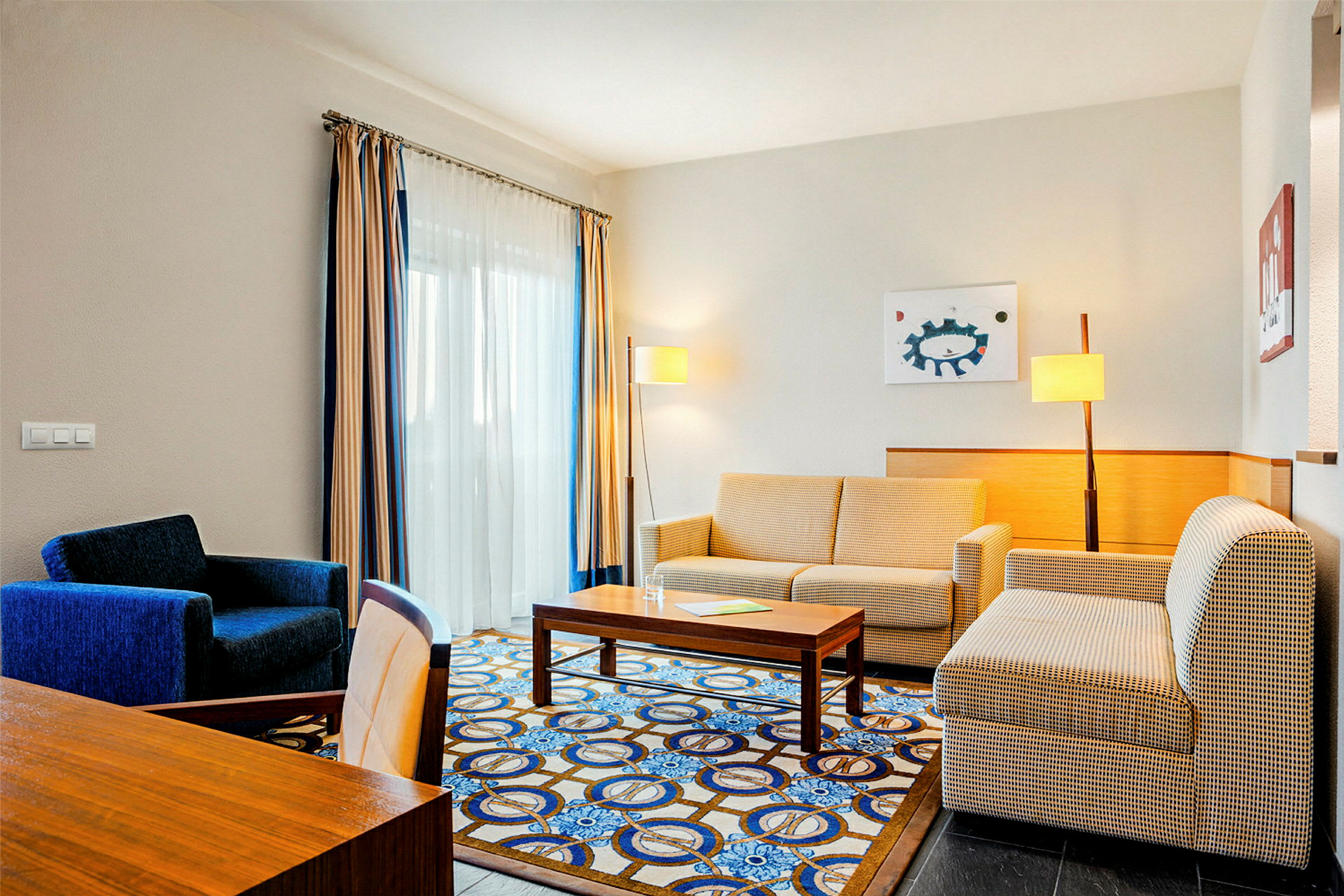 Et hotellrom med sofa, lenestol og bord. (AI-generert tekst)