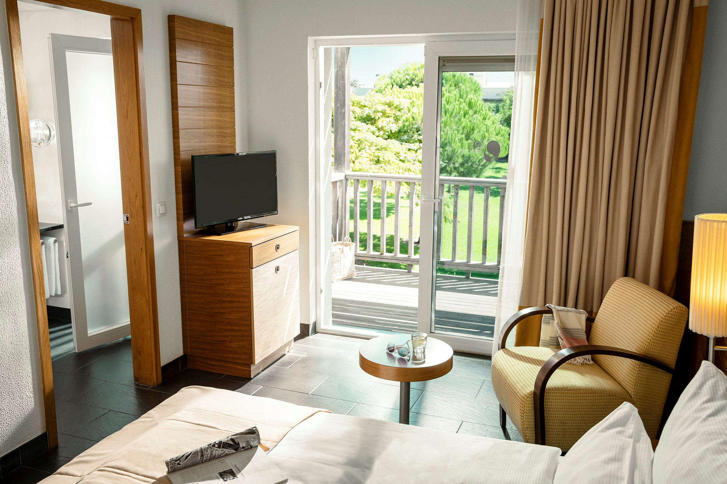 Et hotellrom med en balkong og utsikt over grøntområder utenfor. (AI-generert tekst)