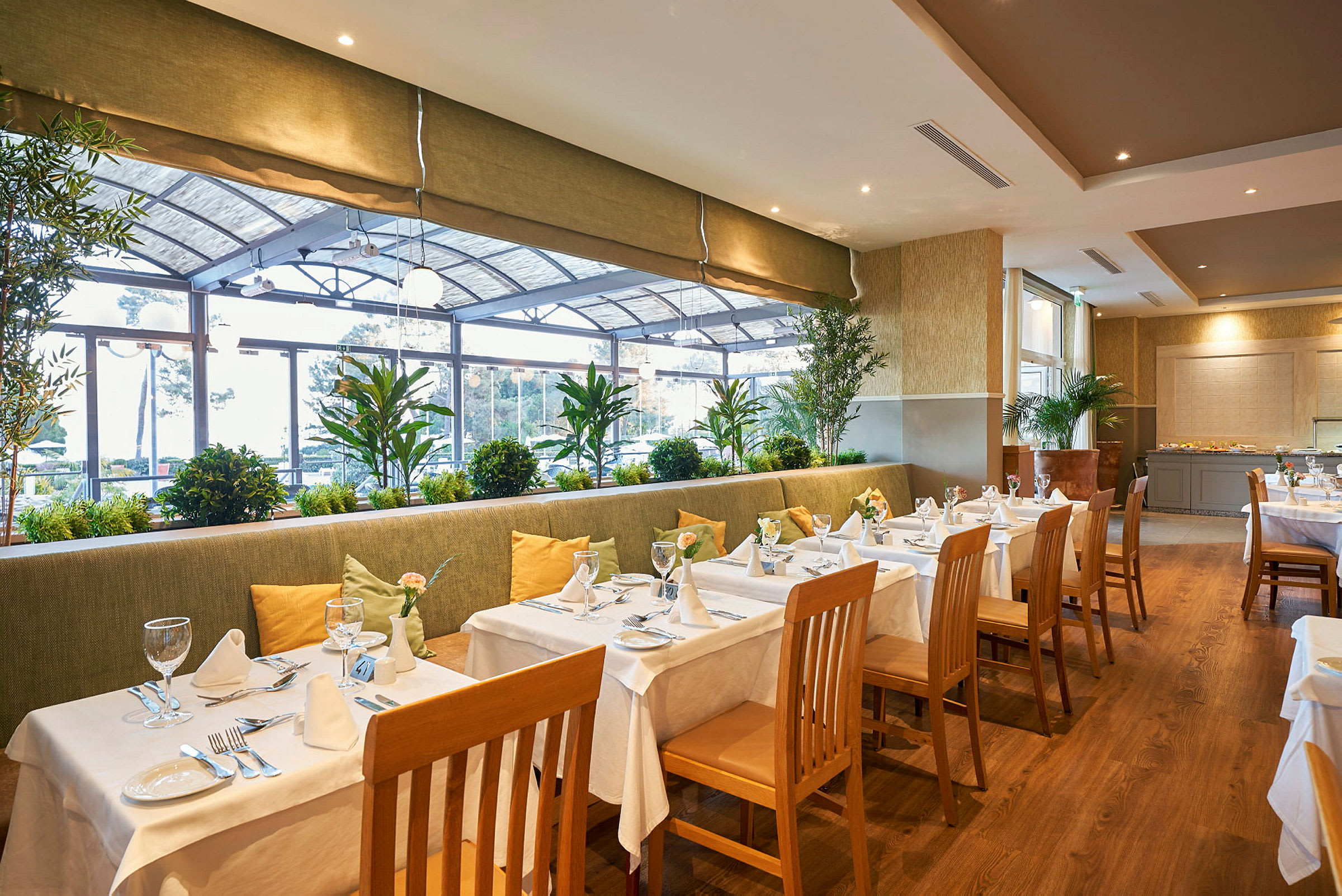 Restaurant med dekket bord, stoler og planter ved vinduet. (AI-generert tekst)