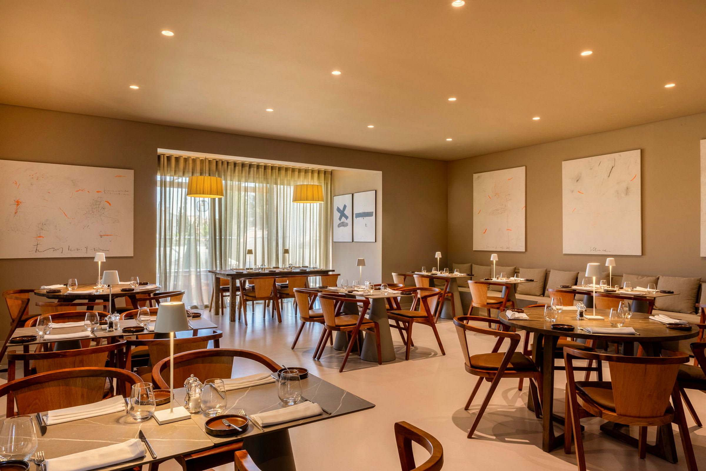 En moderne restaurant med trebord og stoler, dekorativ belysning og kunstverk på veggen. (AI-generert tekst)