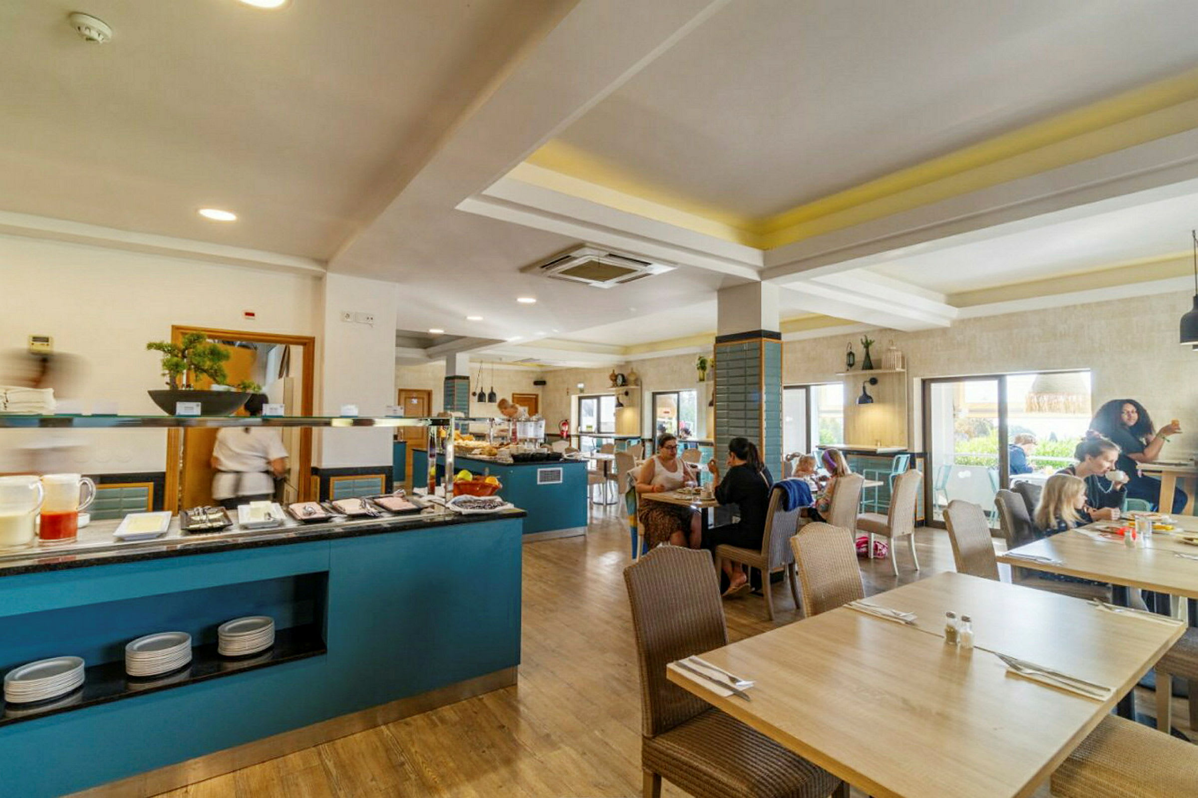 Restaurantmiljø med bord og mennesker, samt en buffédisk med mat og drikke. (AI-generert tekst)