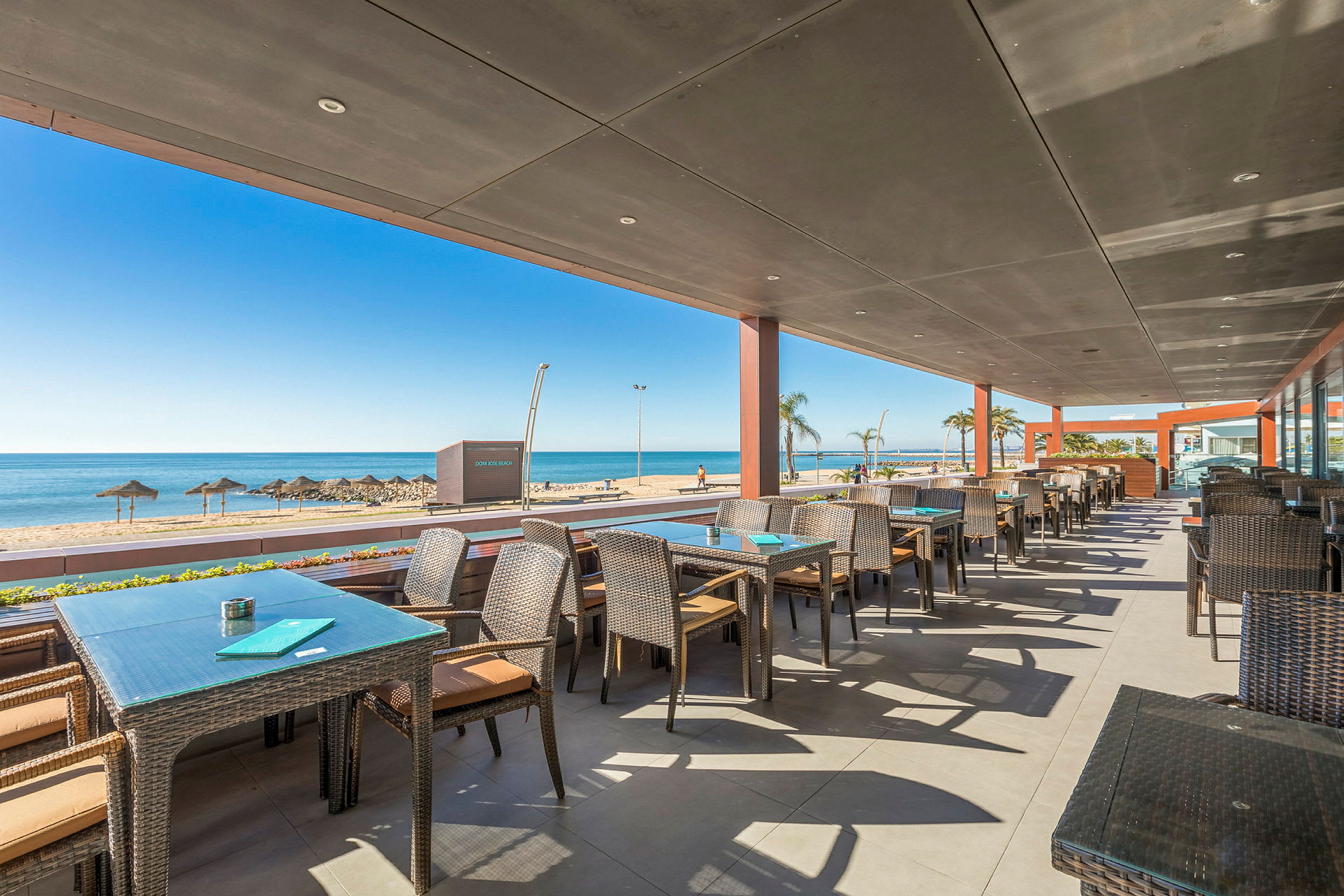 Restaurant med uteservering og utsikt mot stranden og havet. (AI-generert tekst)