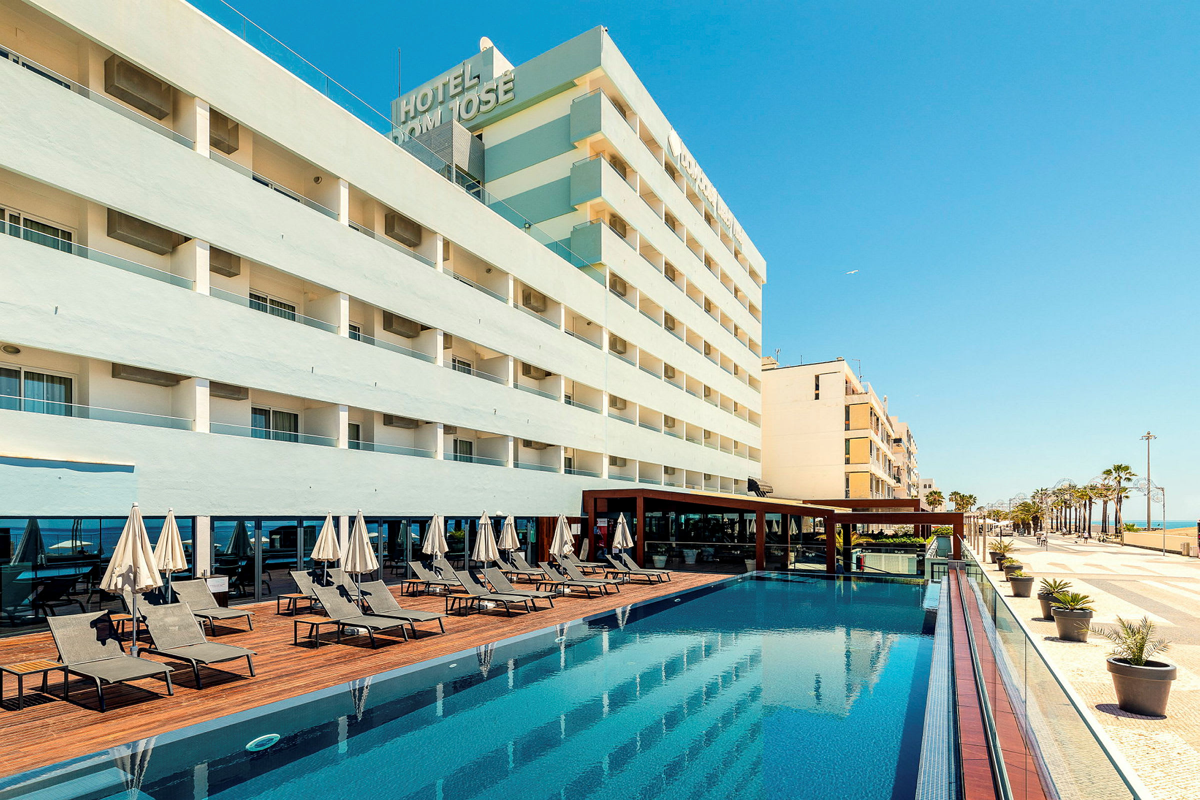 Hotellbygning med basseng og solsenger. (AI-generert tekst)