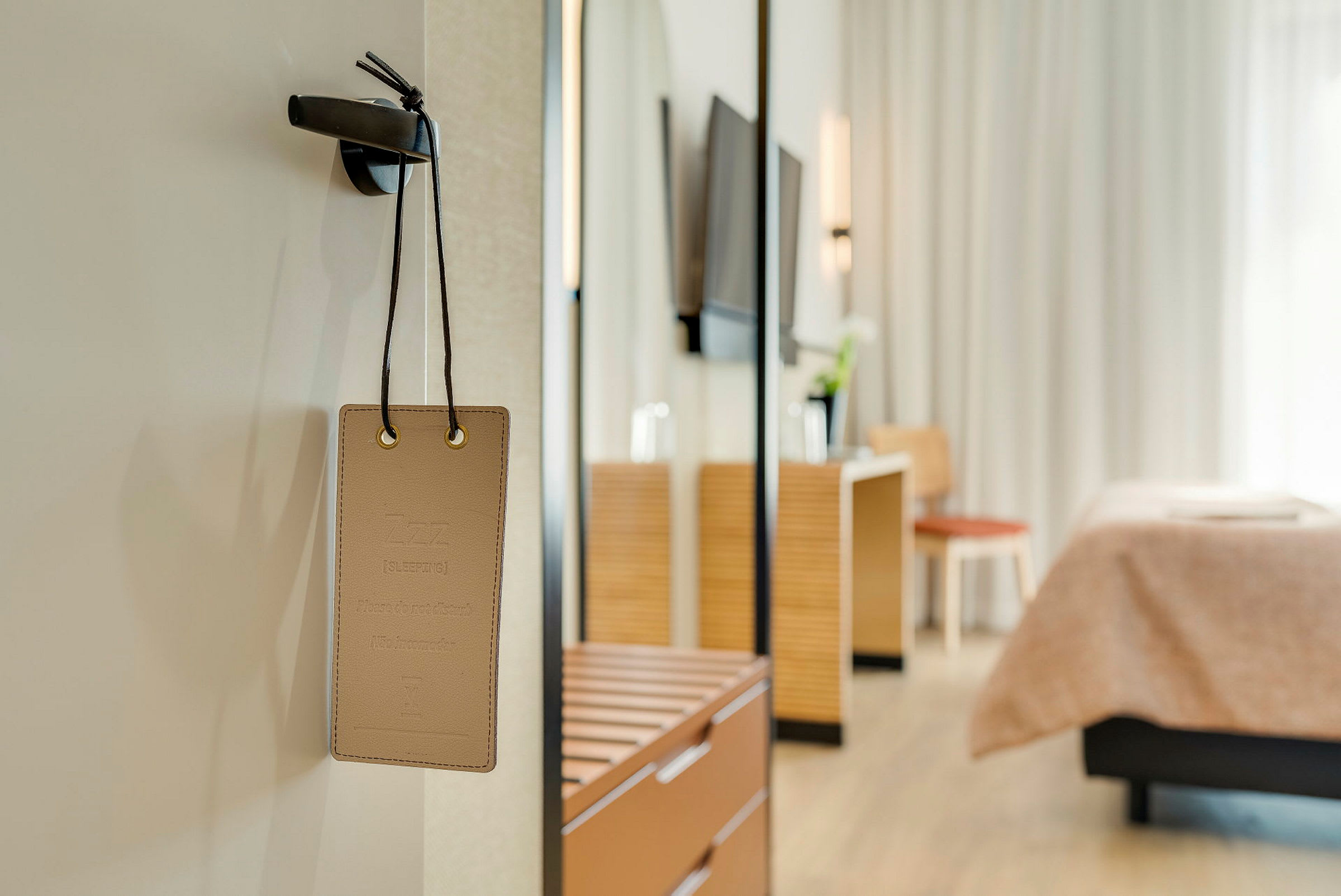 Skilt med teksten 'Sover, ikke forstyrr' hengende på en dør med hotellrominnredning i bakgrunnen. (AI-generert tekst)