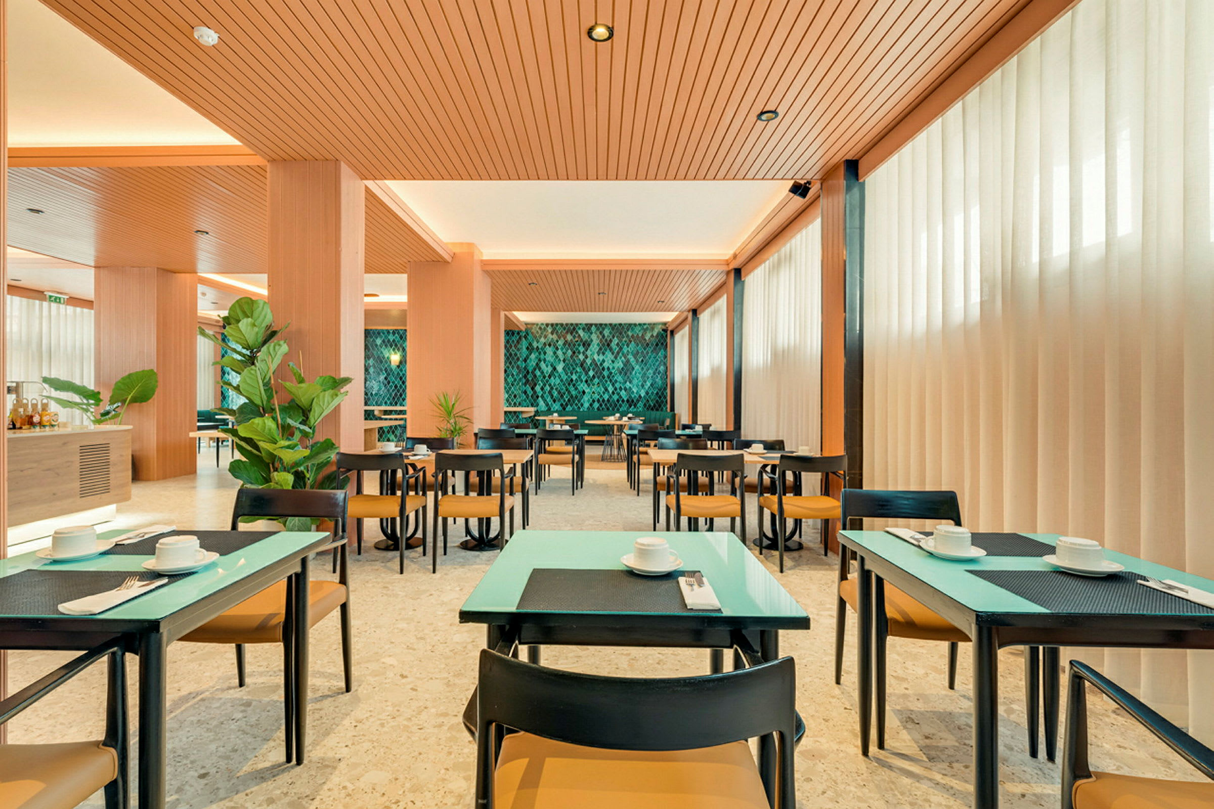 En lys og moderne restaurant med dekkede bord, grønne planter og en dekorativ vegg. (AI-generert tekst)