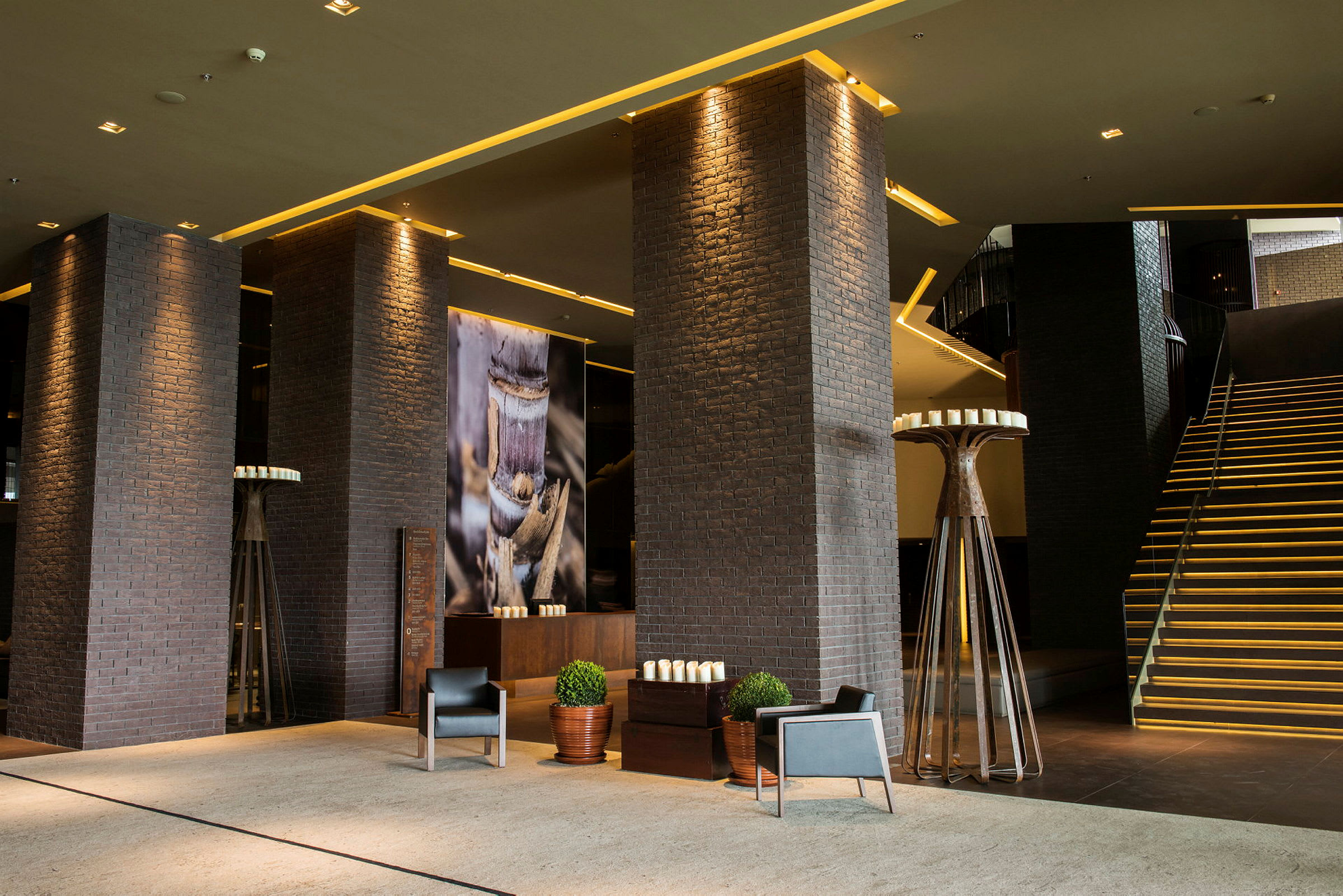 En moderne hotellobby med mørke mursteinsstolper, dekorerte vegger og en opplyst trapp. (AI-generert tekst)