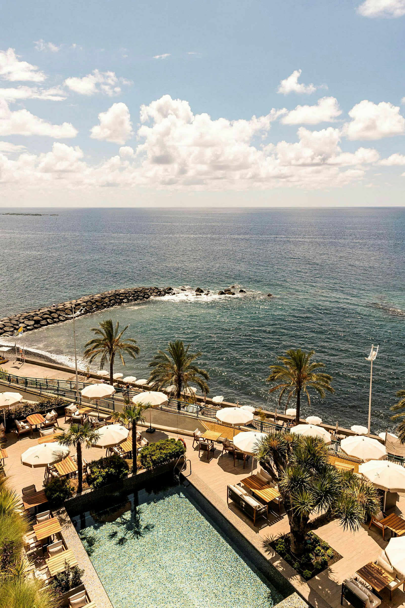 En resort med basseng, parasoller, palmer og utsikt mot havet. (AI-generert tekst)