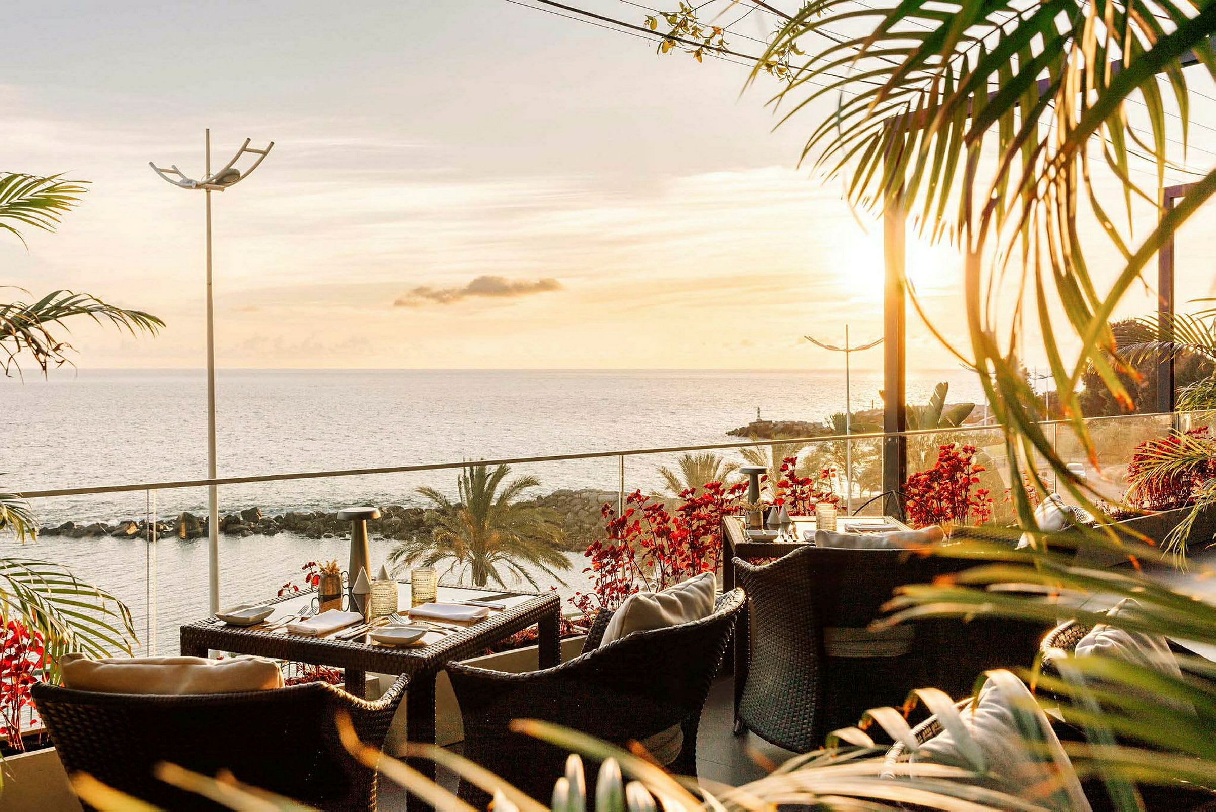 En terrasse med utemøbler og bord, med utsikt over havet og en solnedgang. (AI-generert tekst)