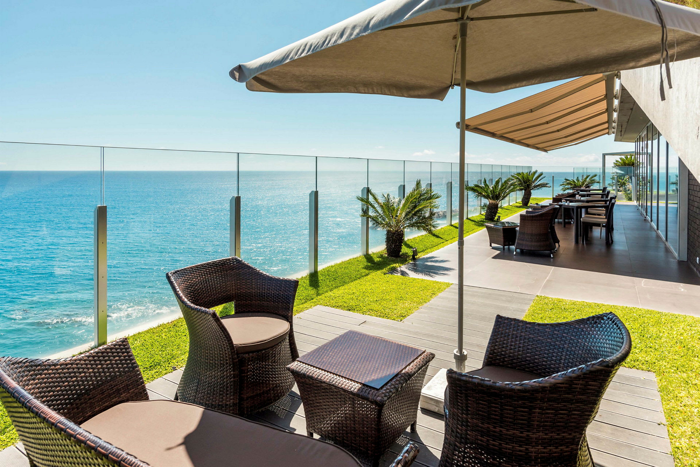 Terrasse med sittemøbler, parasoll og glassrekkverk med utsikt over havet. (AI-generert tekst)