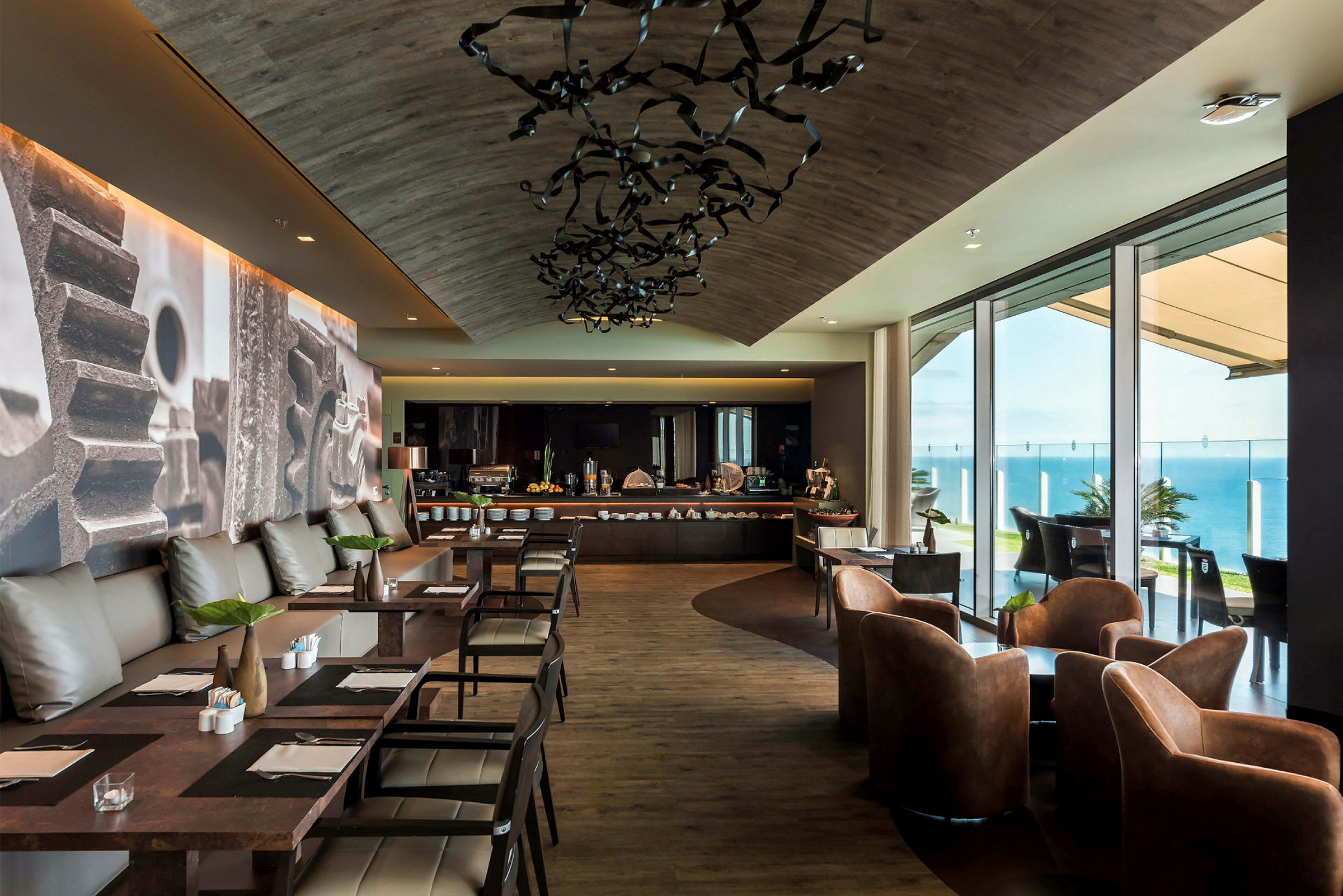 En moderne restaurant med sitteplasser og en buffetbord ved vinduer med utsikt over havet. (AI-generert tekst)
