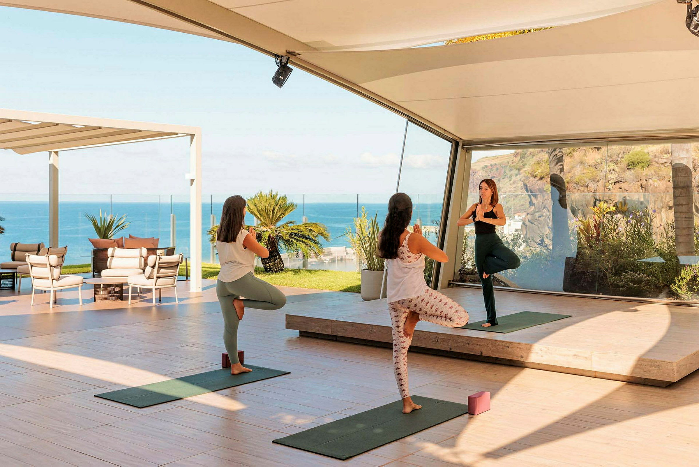 Tre personer utfører yoga i et åpent og lyst miljø med havutsikt. (AI-generert tekst)