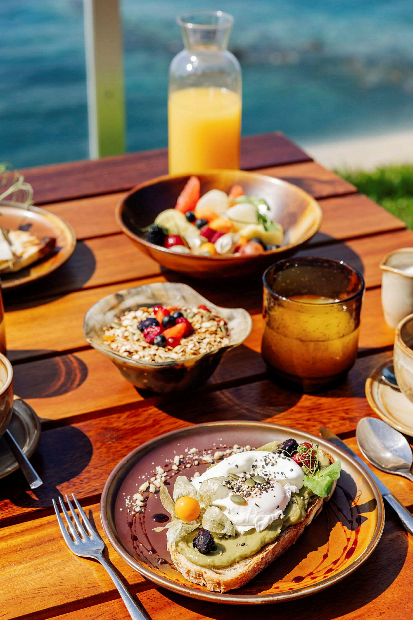 En frokostservering med juice, frukt, granola og avokadosmørbrød. (AI-generert tekst)