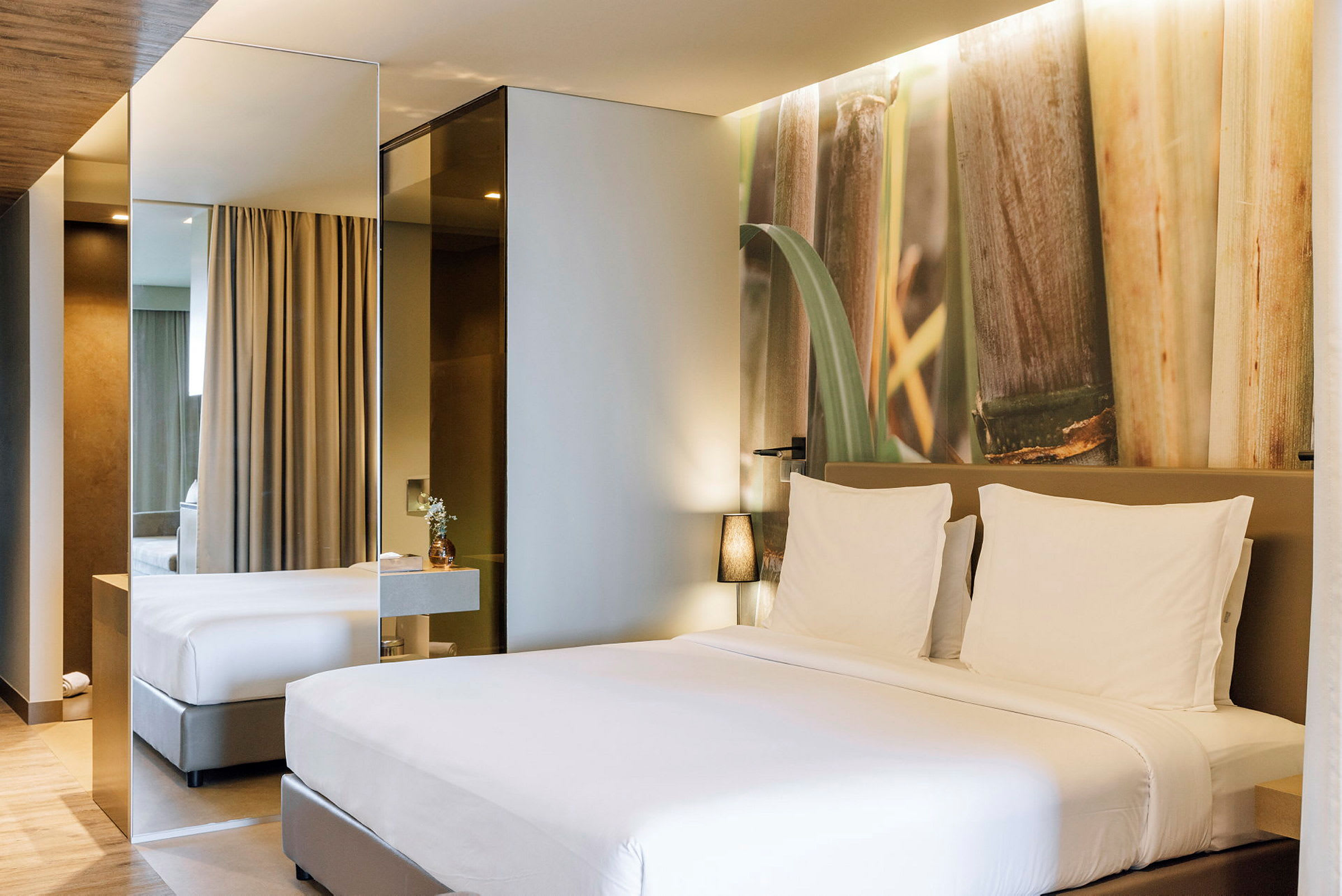 Et moderne hotellrom med en stor seng med hvitt sengetøy og en dekorativ vegg med naturmotiv. (AI-generert tekst)