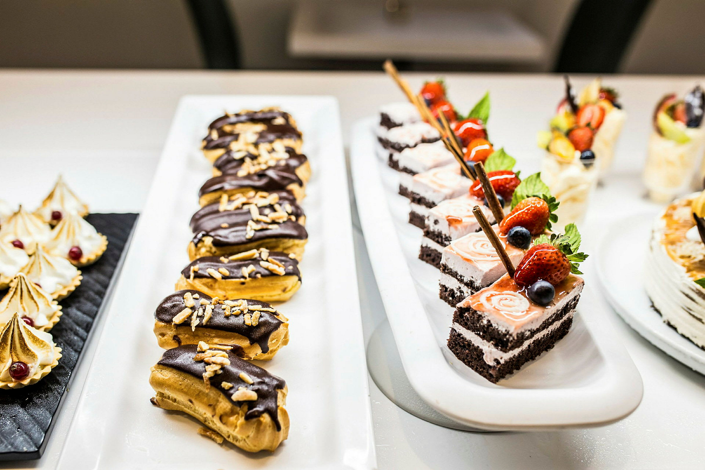 Et bord med forskjellige desserter, inkludert sjokoladetrekte eclairs og kakebiter med fruktdekor. (AI-generert tekst)