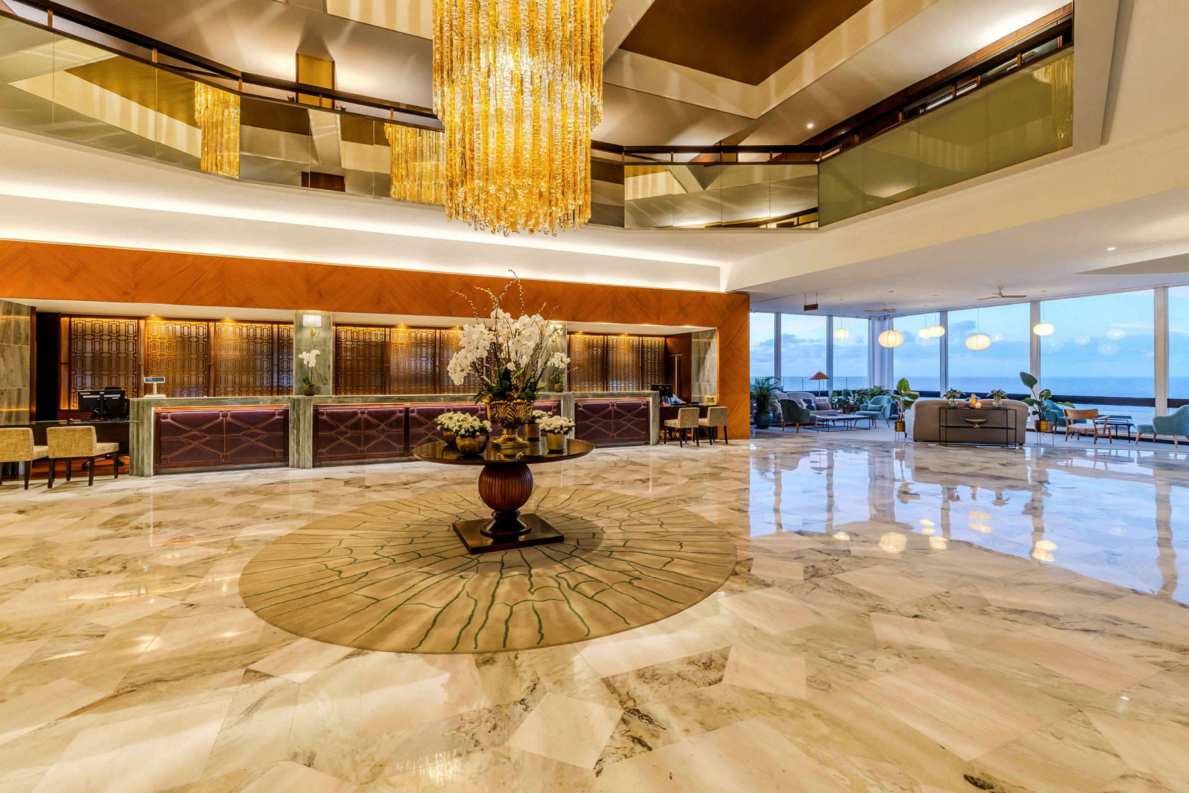 En elegant hotellobby med et stort gulv i marmor, en sentral dekorasjon med blomster og en krystallkrone som henger fra taket. (AI-generert tekst)