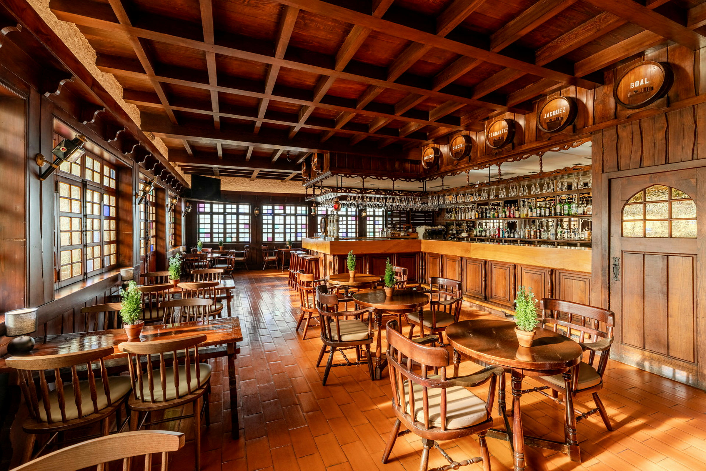 Interiør av en rustikk restaurant med trepaneler, trebord og stoler samt en bardisk med glass og flasker. (AI-generert tekst)