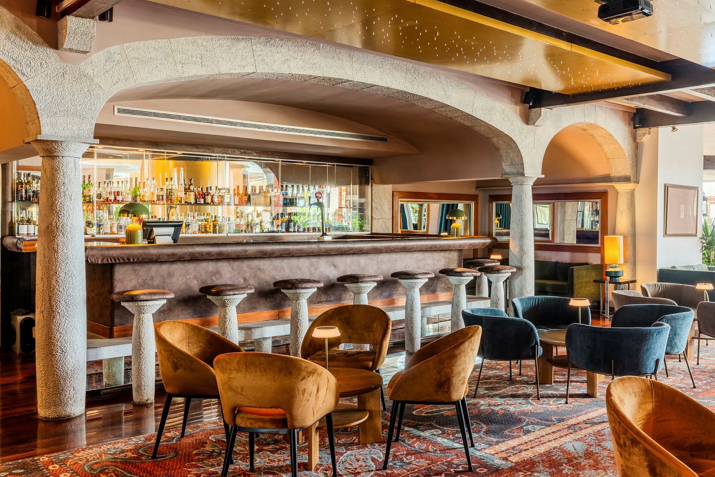 Bilde av en elegant bar med en bardisk omgitt av høye barstoler samt sitteplasser med sofaer og stoler i et stilfullt innredet område. (AI-generert tekst)