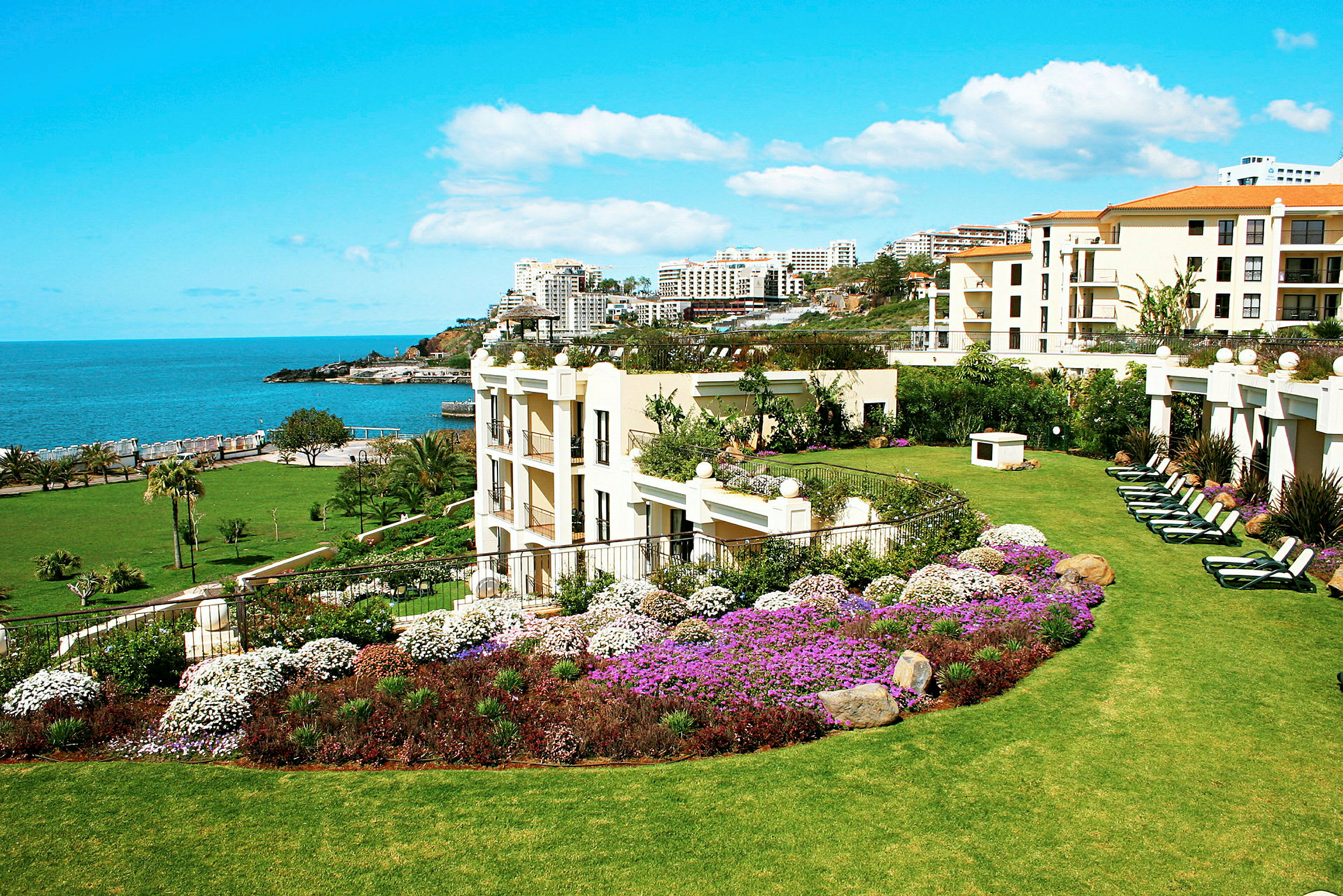Grønn hotellhage med blomster og utsikt mot havet. (AI-generert tekst)