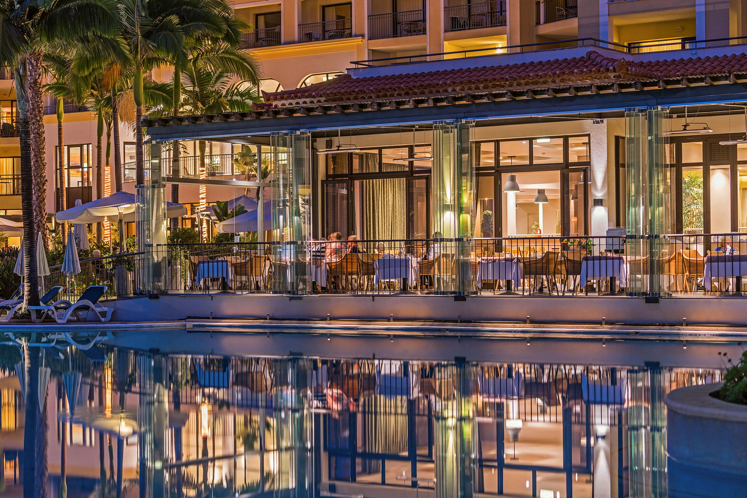 En belyst restaurant ved et basseng og hotellfasade om kvelden. (AI-generert tekst)