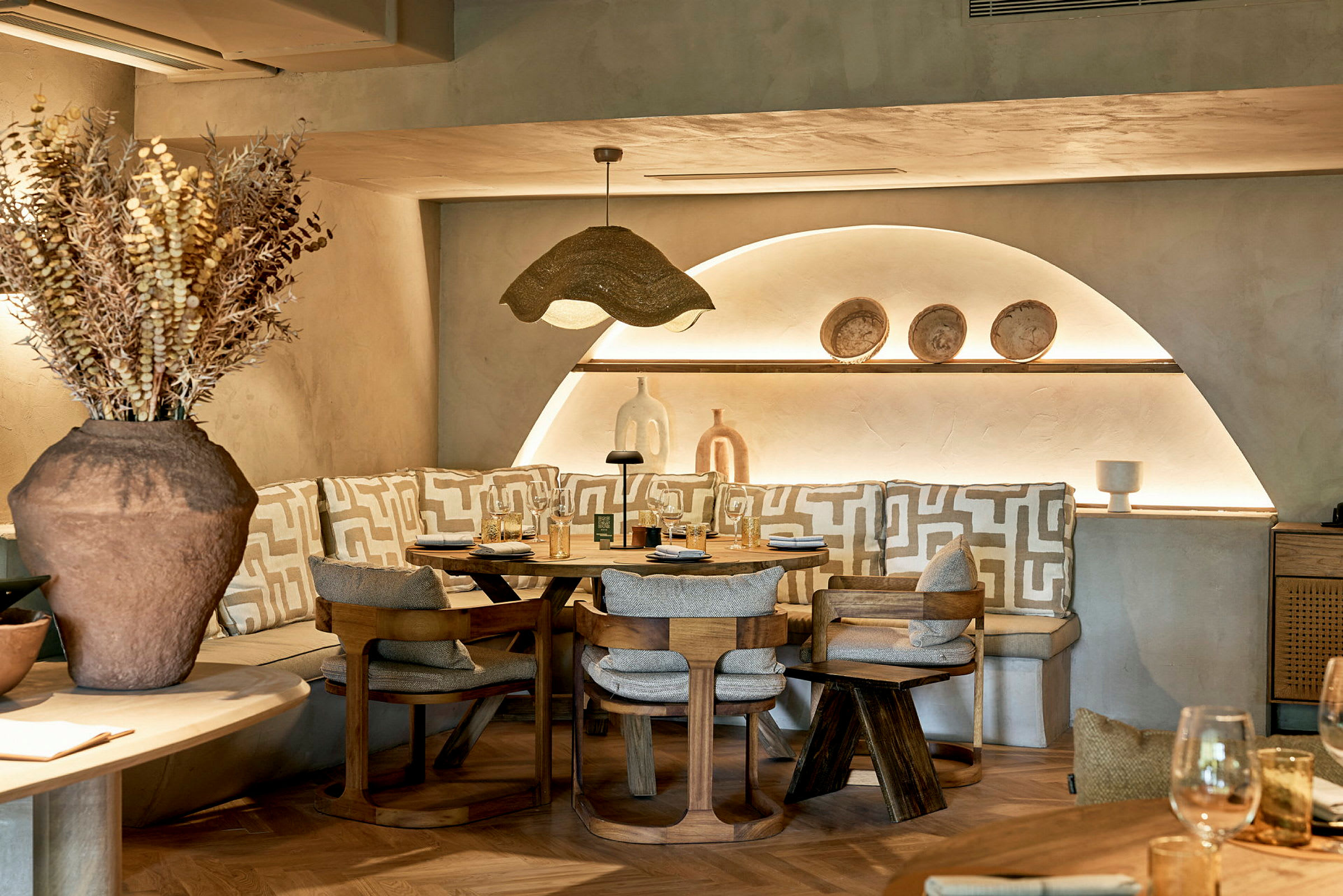 Et stilfullt restaurantbord omgitt av stoler og benker med geometriske mønstrede puter. (AI-generert tekst)