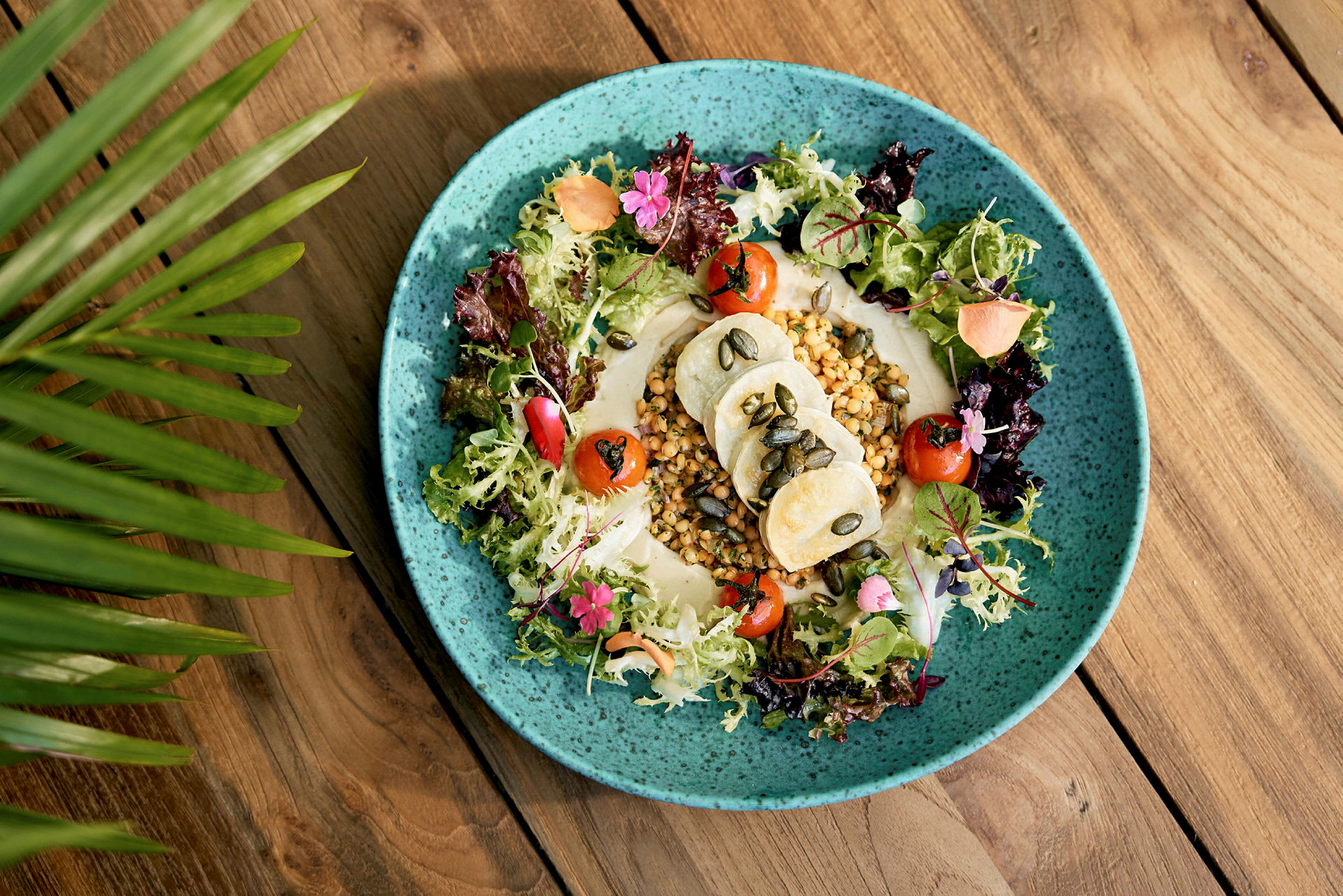 En tallerken med salat, grønnsaker og hummus på et bord. (AI-generert tekst)