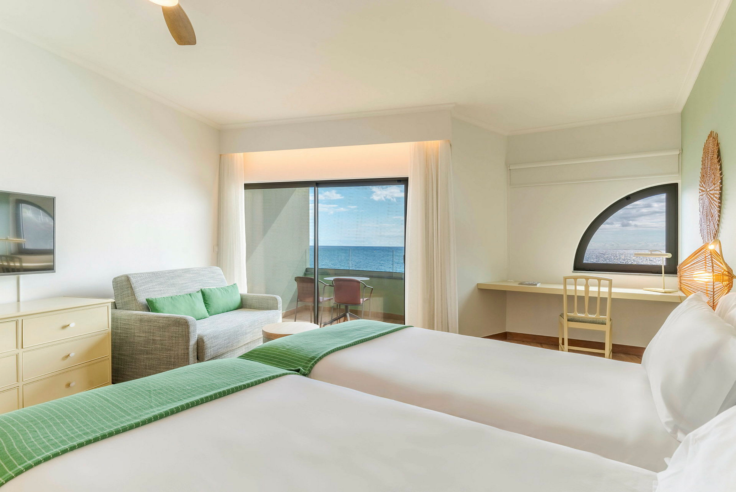 Hotellrom med to senger, en sofa, et skrivebord og en balkong med havutsikt. (AI-generert tekst)