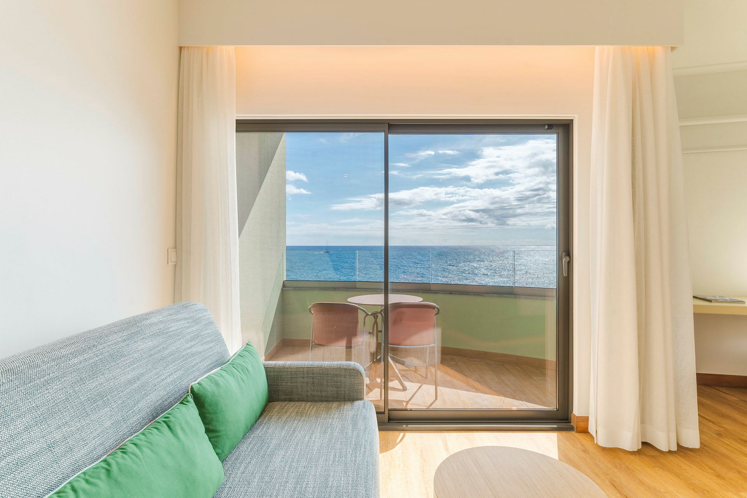 Et hotellrom med en sofa og utsikt mot en balkong med havet i bakgrunnen. (AI-generert tekst)