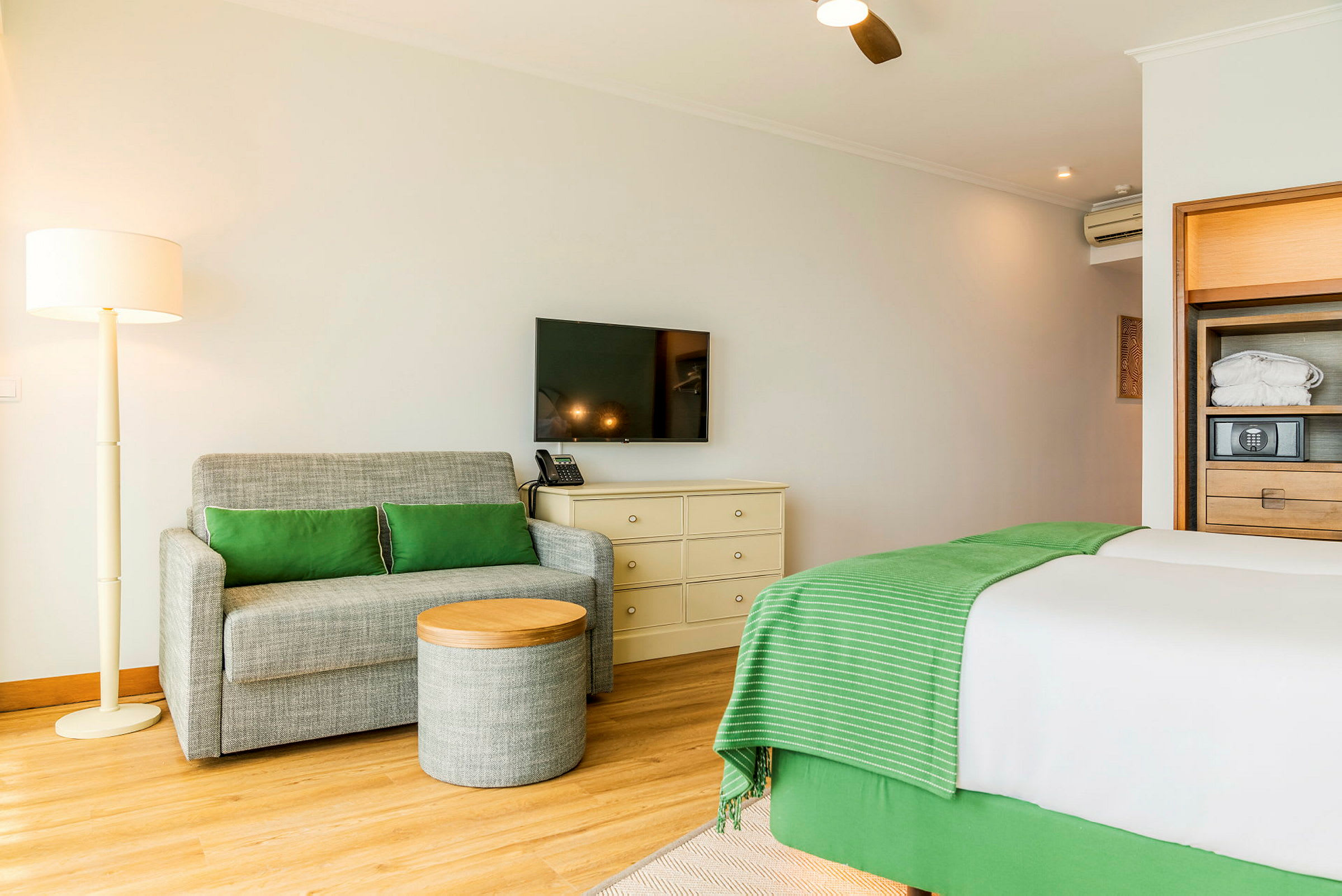 Et hotellrom med en sofa, et lite bord, en seng og en TV på veggen. (AI-generert tekst)