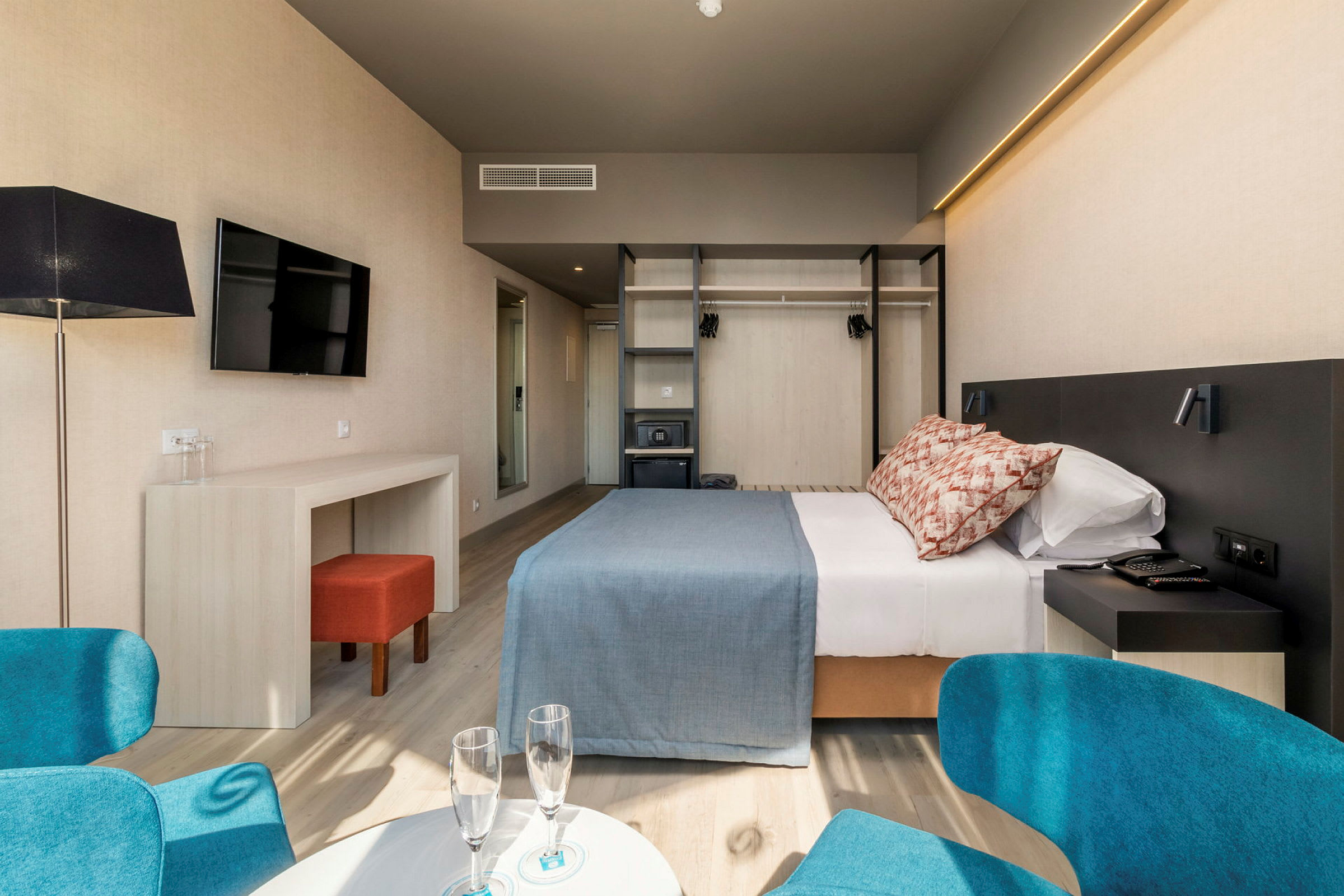 Et hotellrom med dobbeltseng, skrivebord, stol og garderobe. (AI-generert tekst)